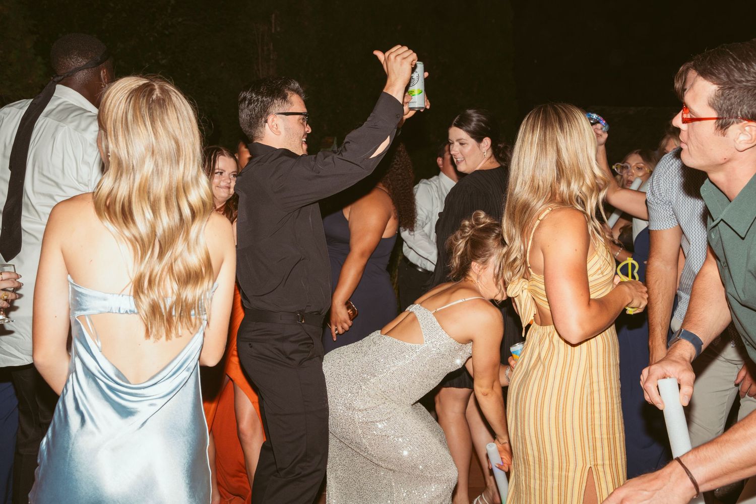 People dancing and socializing at a crowded party or nightclub in a dark setting with dim lighting.