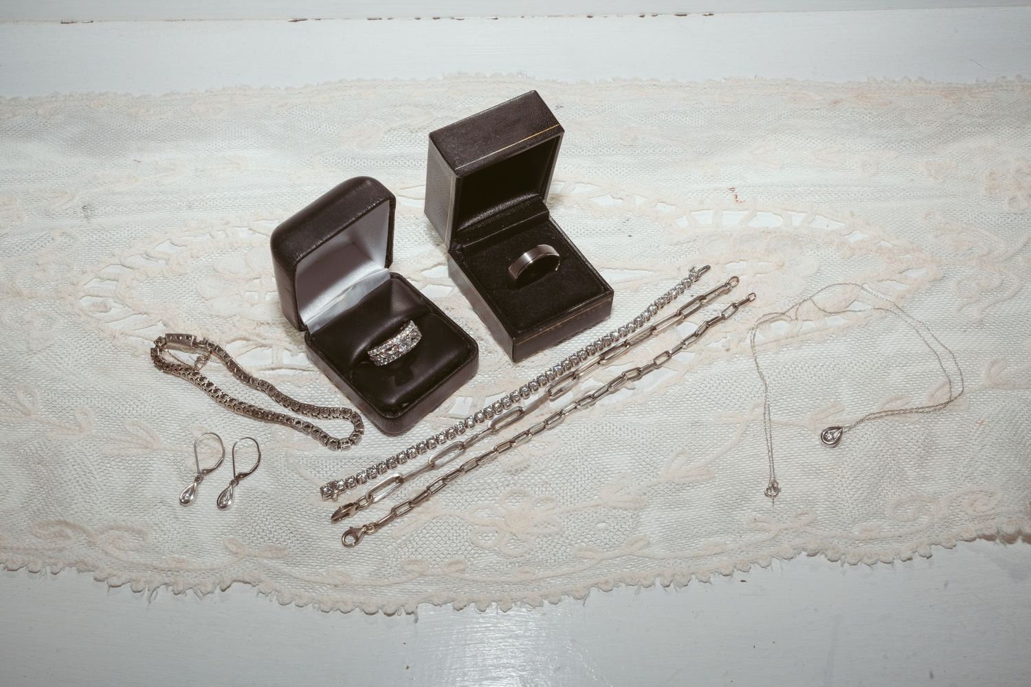 Elegant jewelry pieces including necklaces and rings displayed in dark wooden boxes on a white surface.
