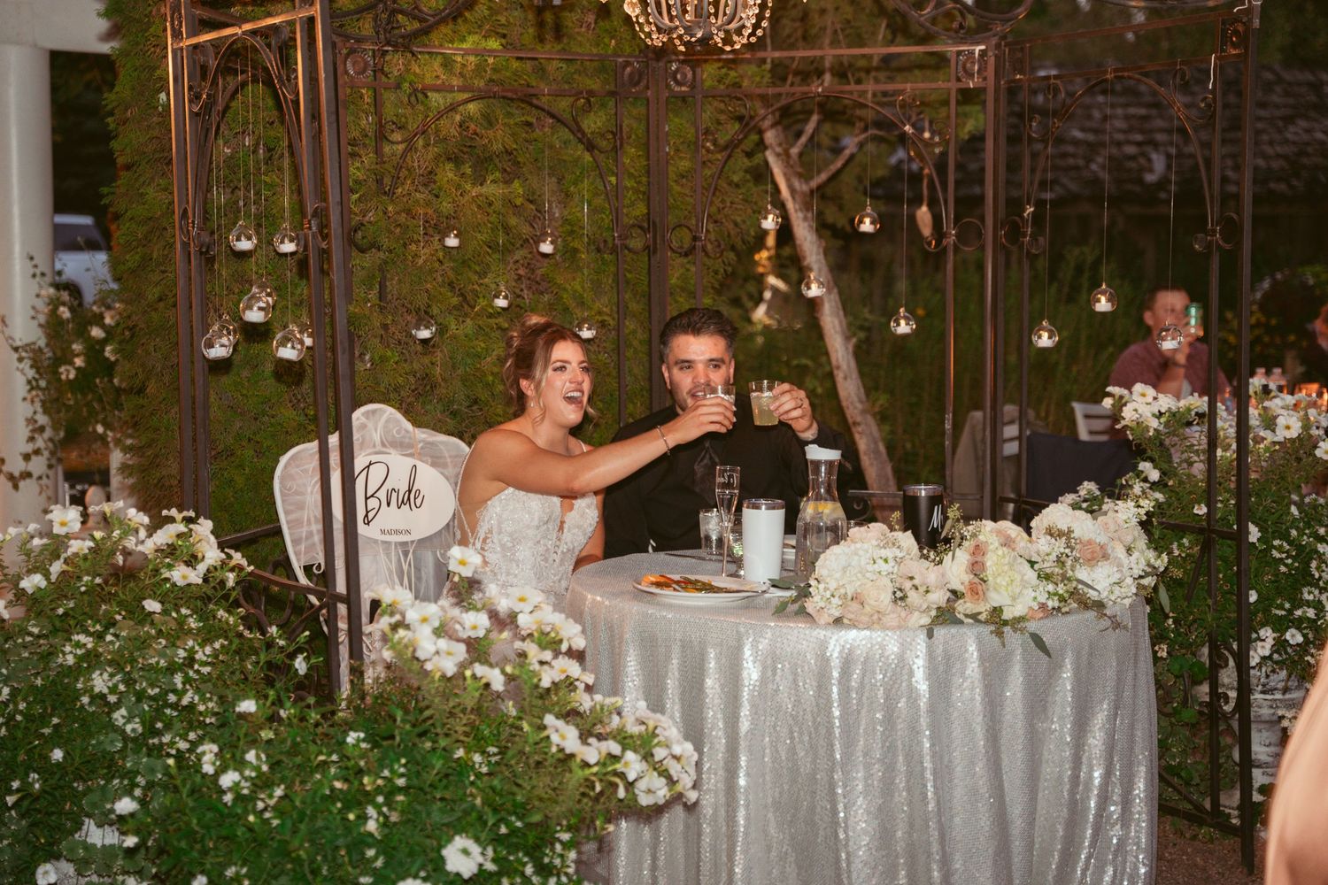 Elegant wedding reception setup with chandeliers and floral centerpieces in an outdoor garden setting.