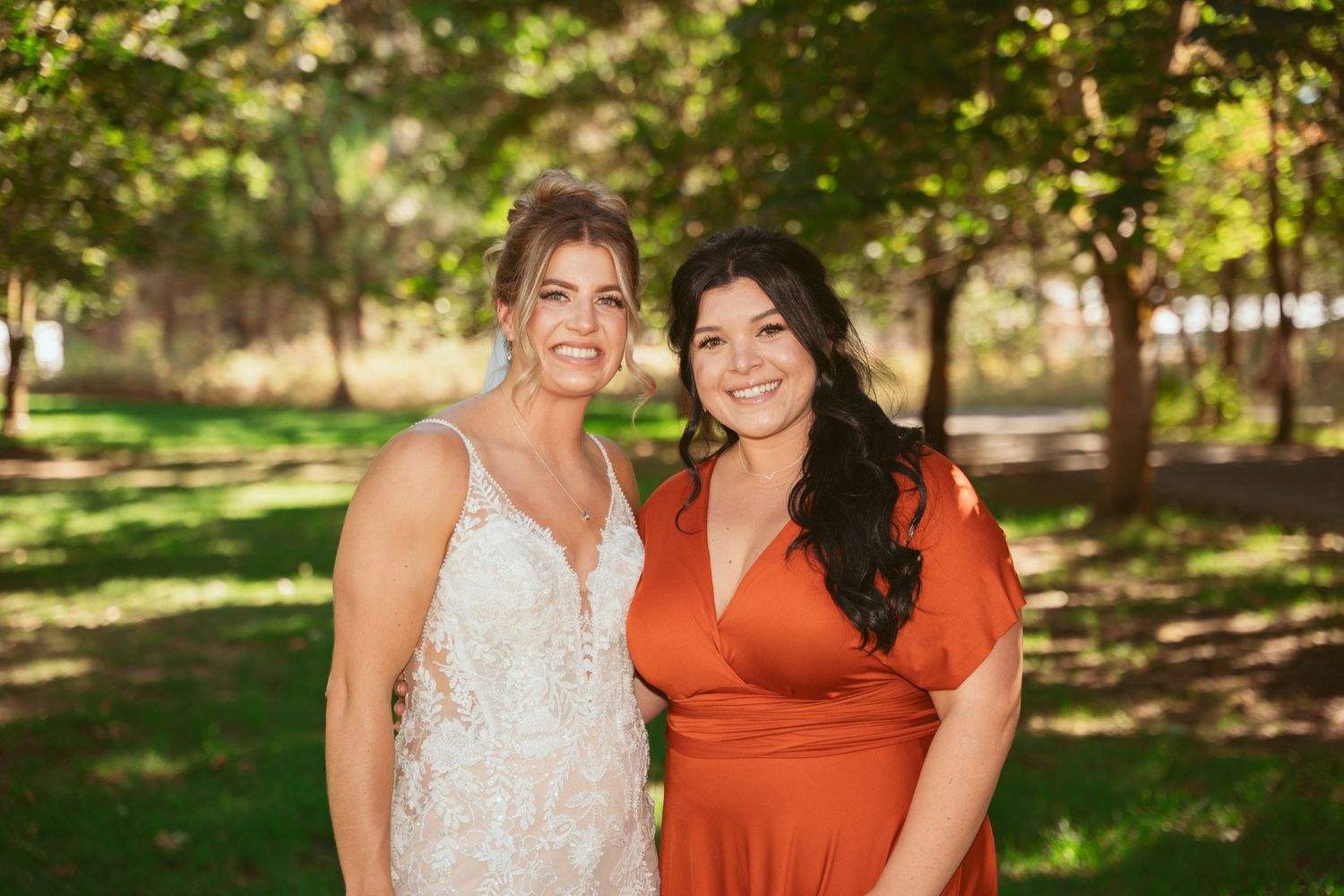 Wedding party members in white and orange dresses pose together on a sunny lawn.