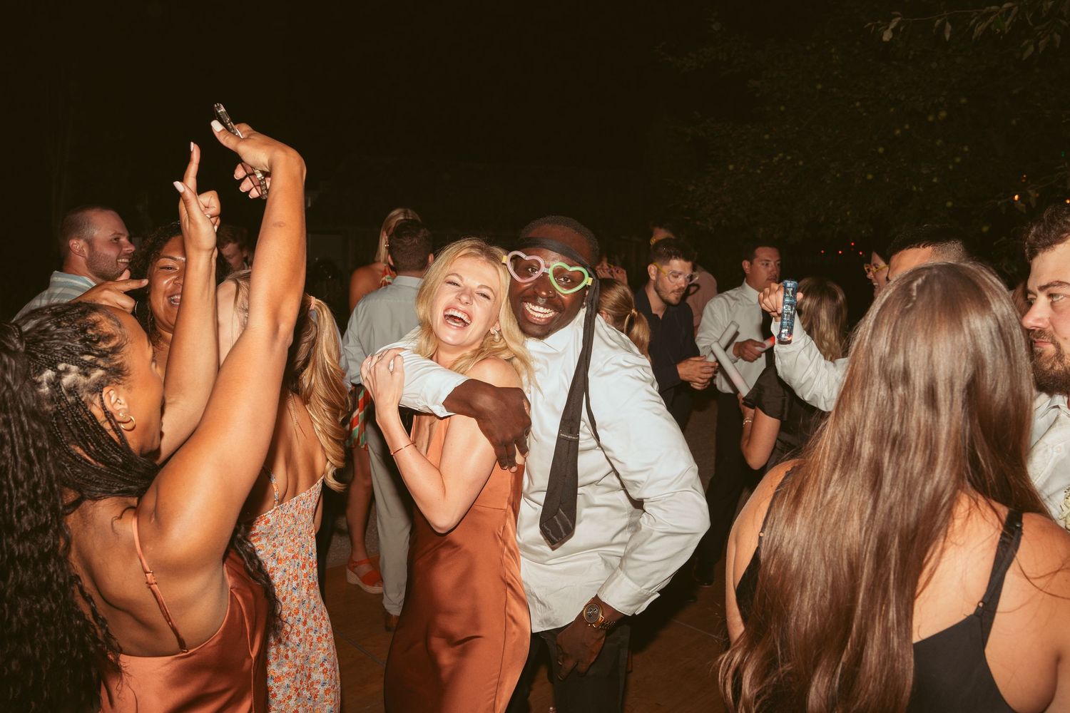 Wedding guests dance energetically on a wooden dance floor during the evening reception.