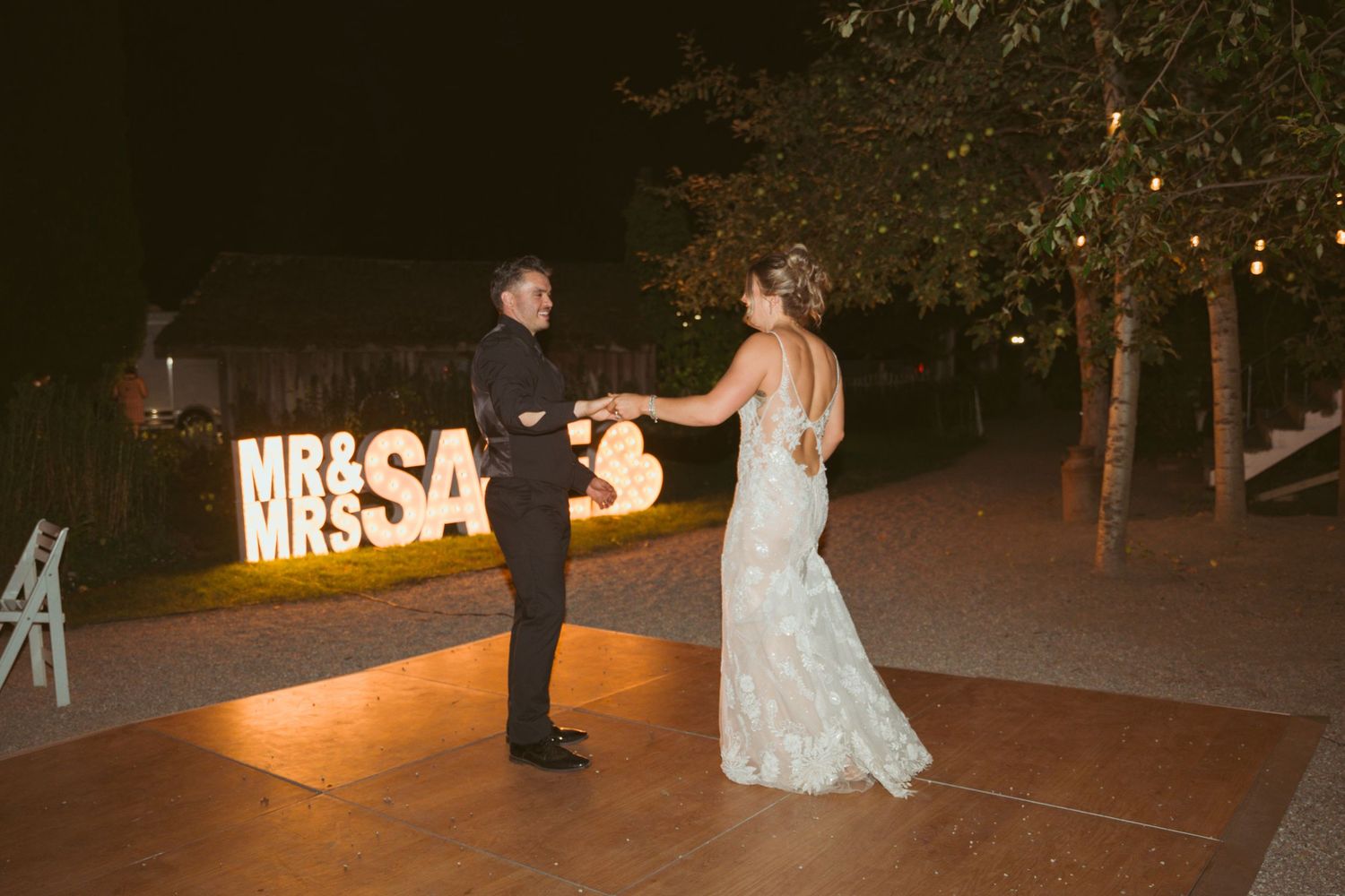 Couple dancing together near illuminated wedding sign during evening reception.