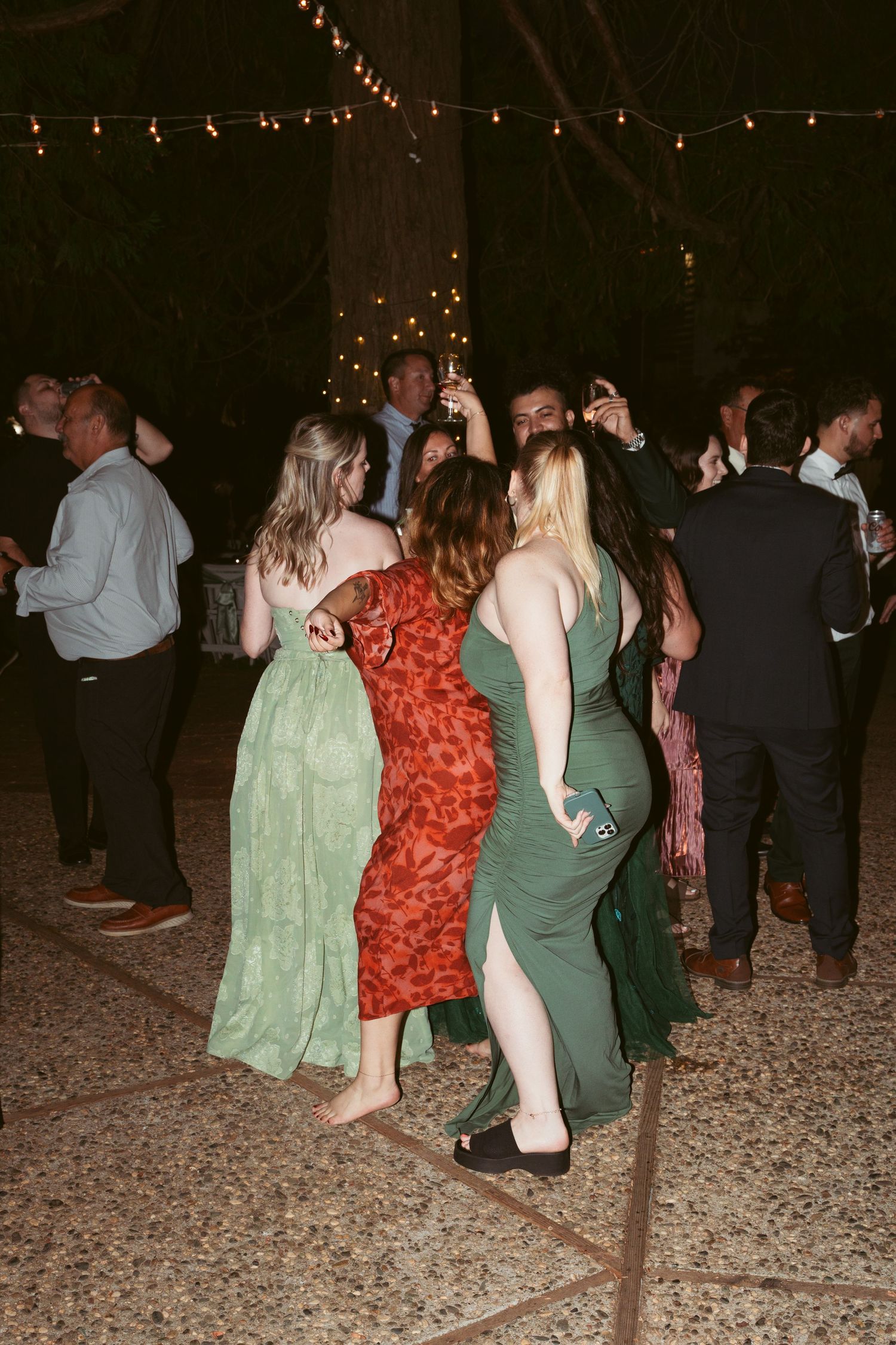 Wedding guests dancing under string lights at an outdoor nighttime reception.