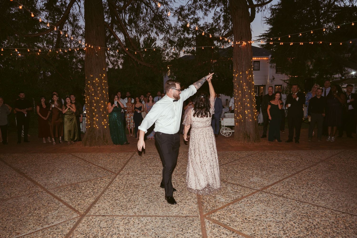 A couple performs a playful dance move during their wedding reception on an outdoor patio.