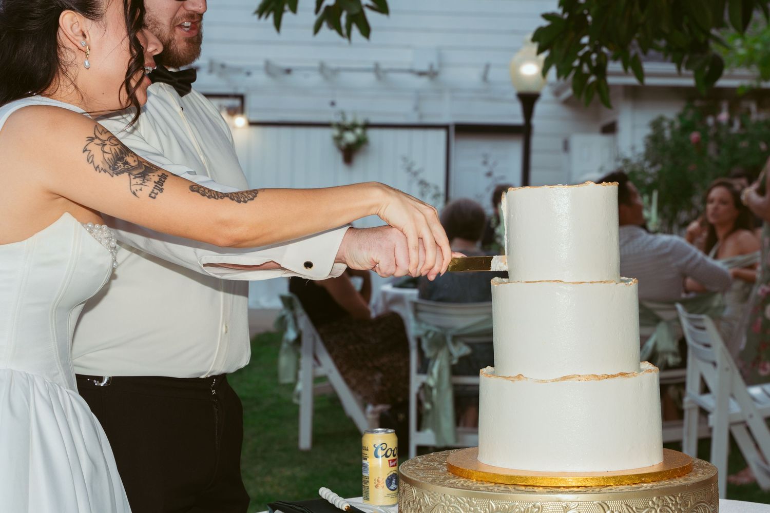 A couple slices their wedding cake together on a gold cake stand during their reception.