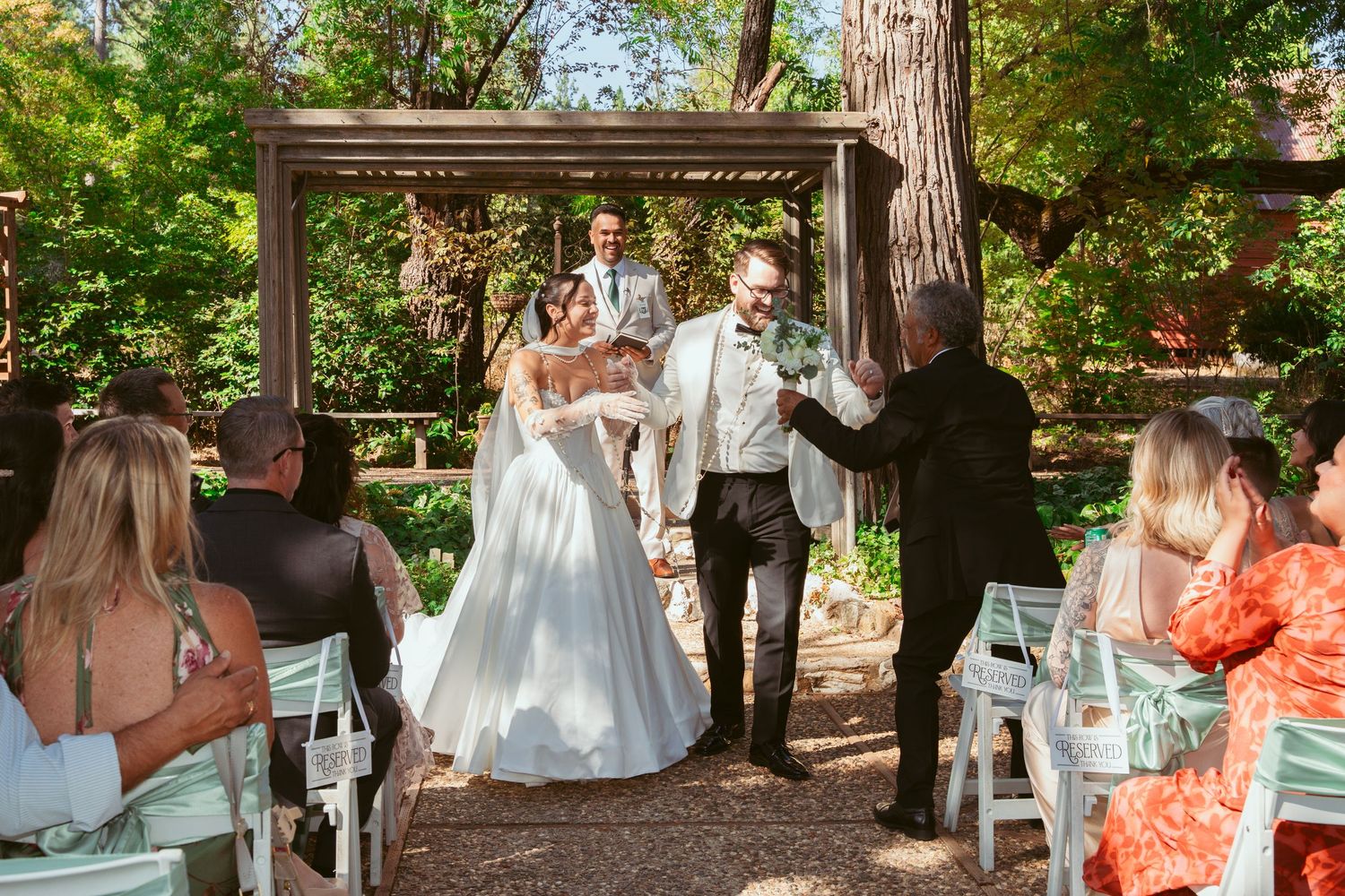 Wedding celebration sequence with guests and party members under wooden outdoor structure.
