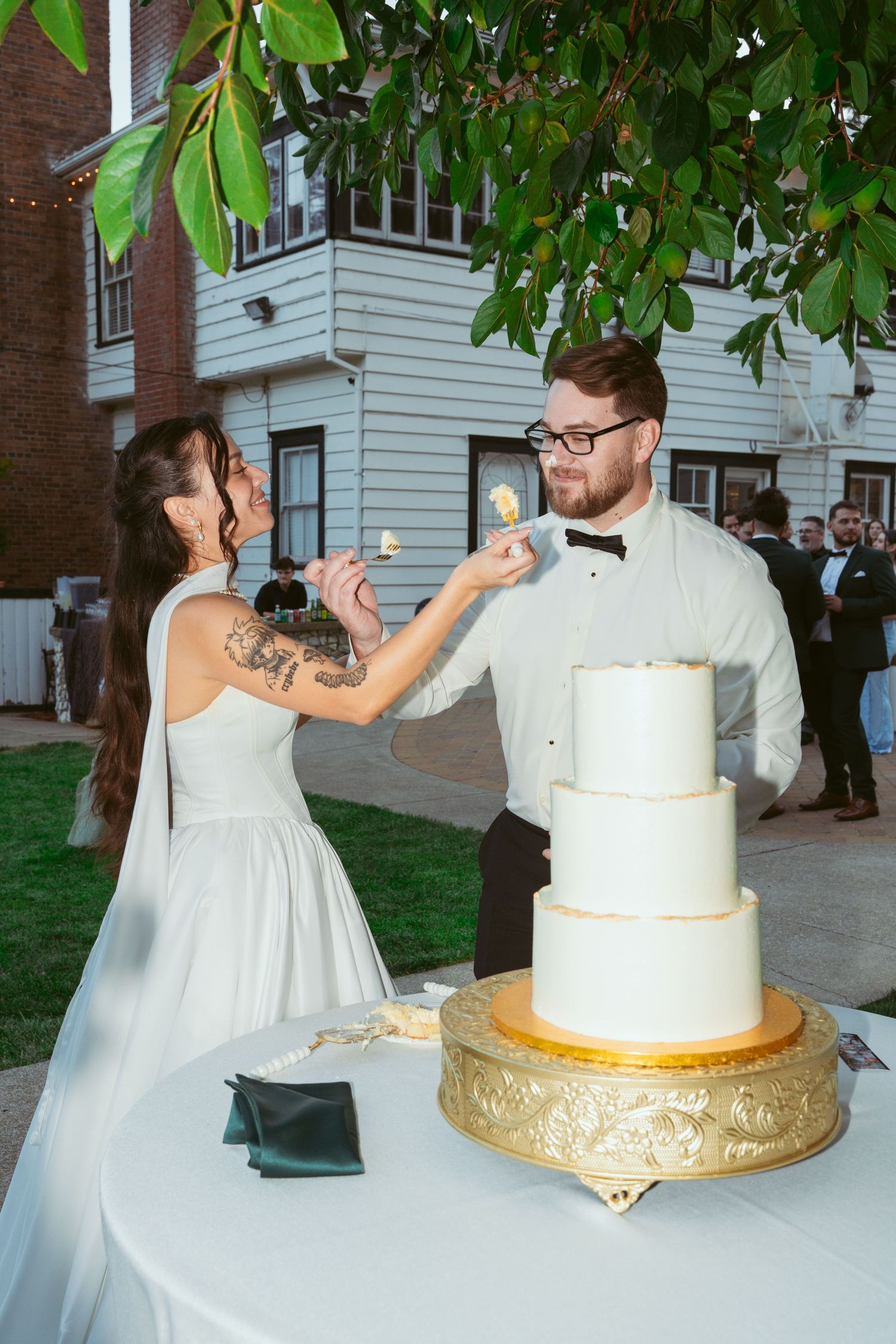 A couple playfully feeds each other wedding cake during their outdoor reception celebration.