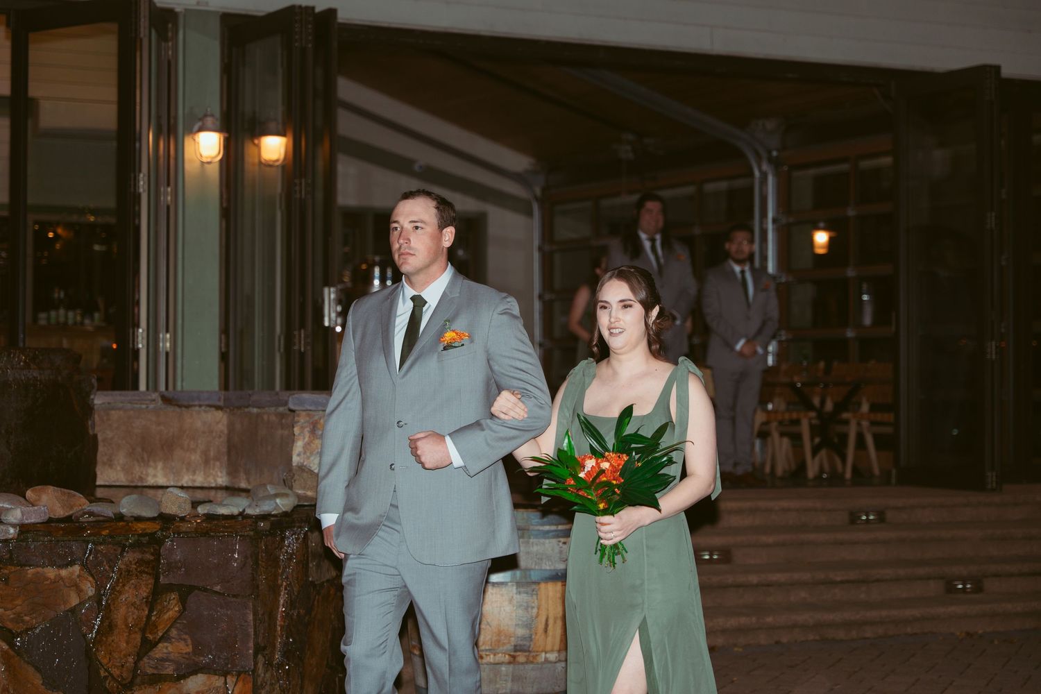 Wedding party members pose together under outdoor lighting at dusk.