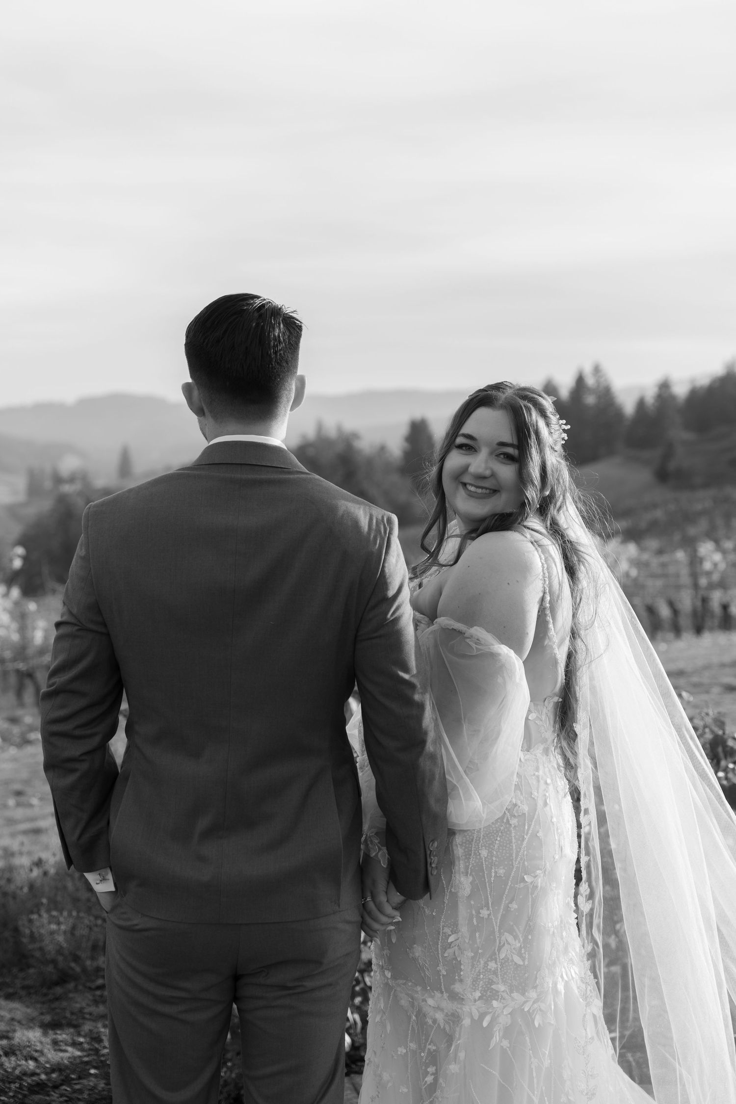 Black and white wedding portrait capturing candid moment in vineyard setting.