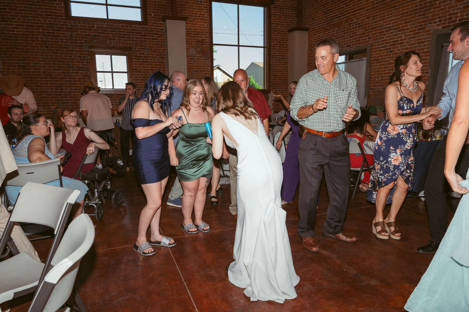 Wedding party dancing and celebrating in an industrial-style venue with brick walls and large windows.