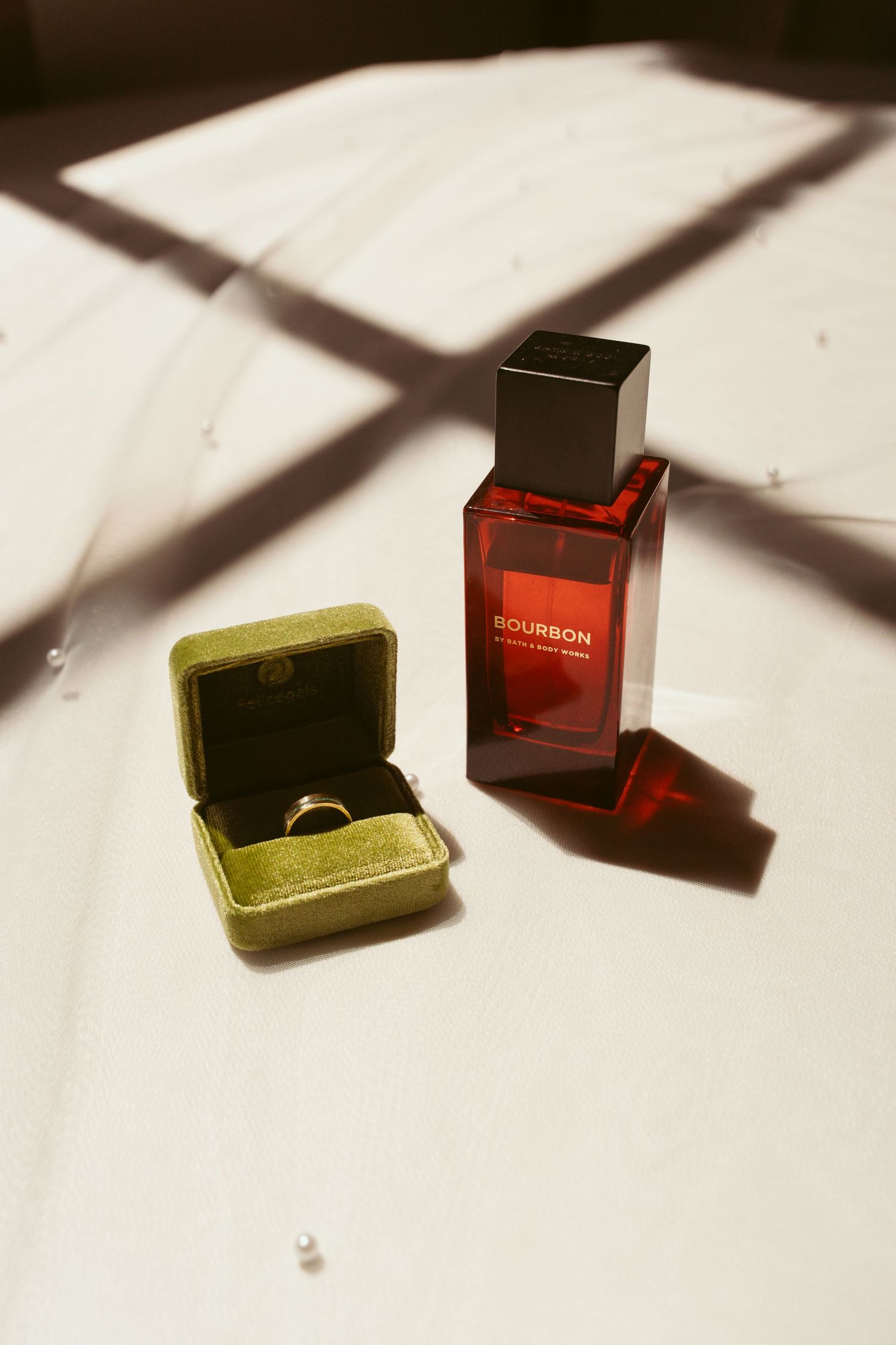 A red perfume bottle and velvet ring box casting dramatic shadows on a white surface.