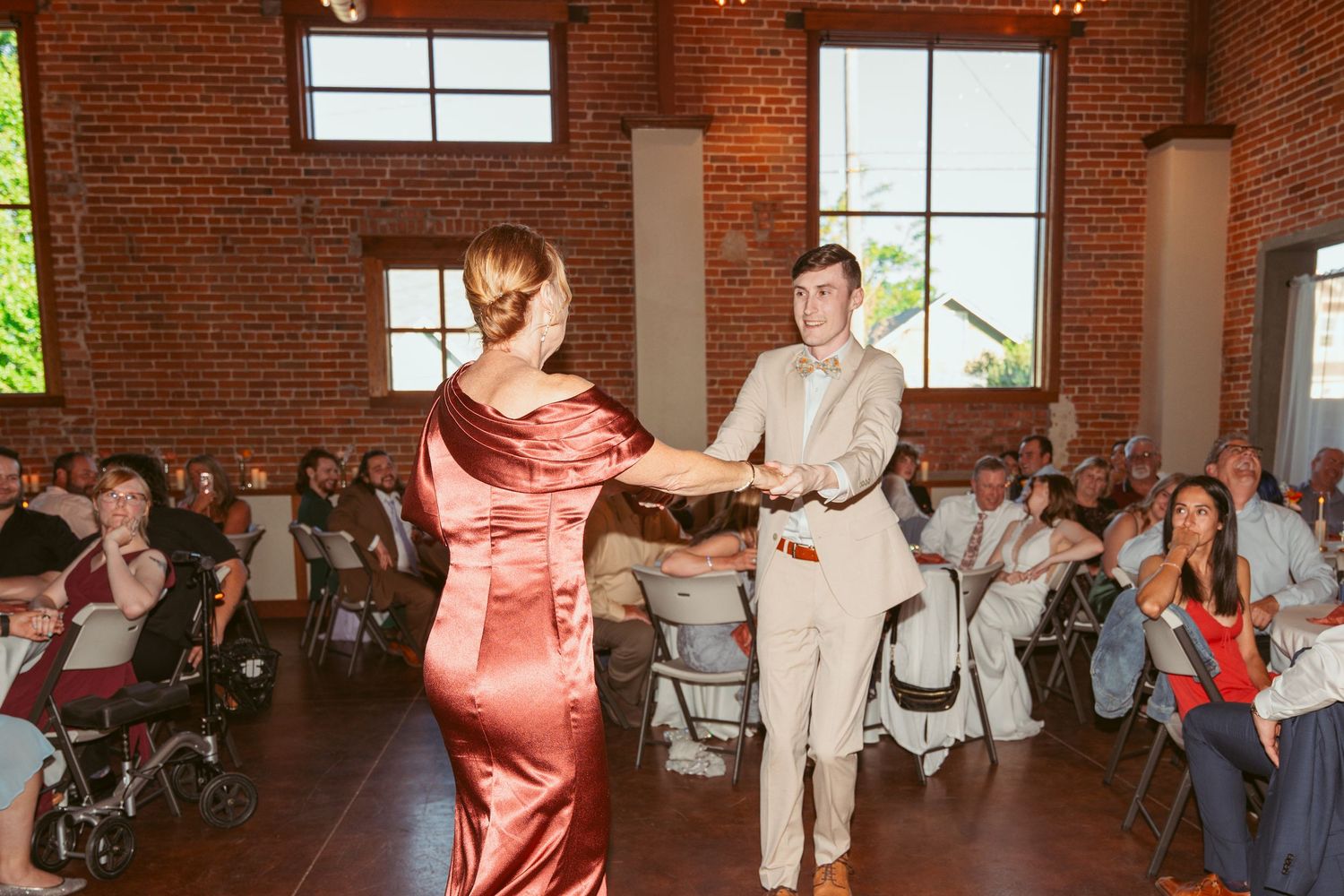 Couple dancing together at a wedding reception in a rustic brick venue with string lights overhead.