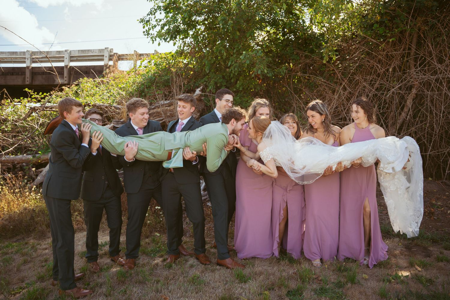 Fun wedding party photo with members leaning and posing creatively in a row outdoors.