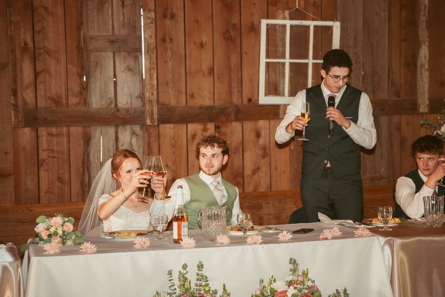 Wedding speeches and toasts during reception dinner in rustic barn venue with wooden paneled walls.