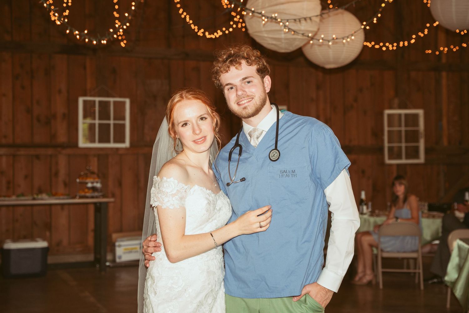 Couples dancing together at a wedding reception in a warmly lit barn with string lights overhead.