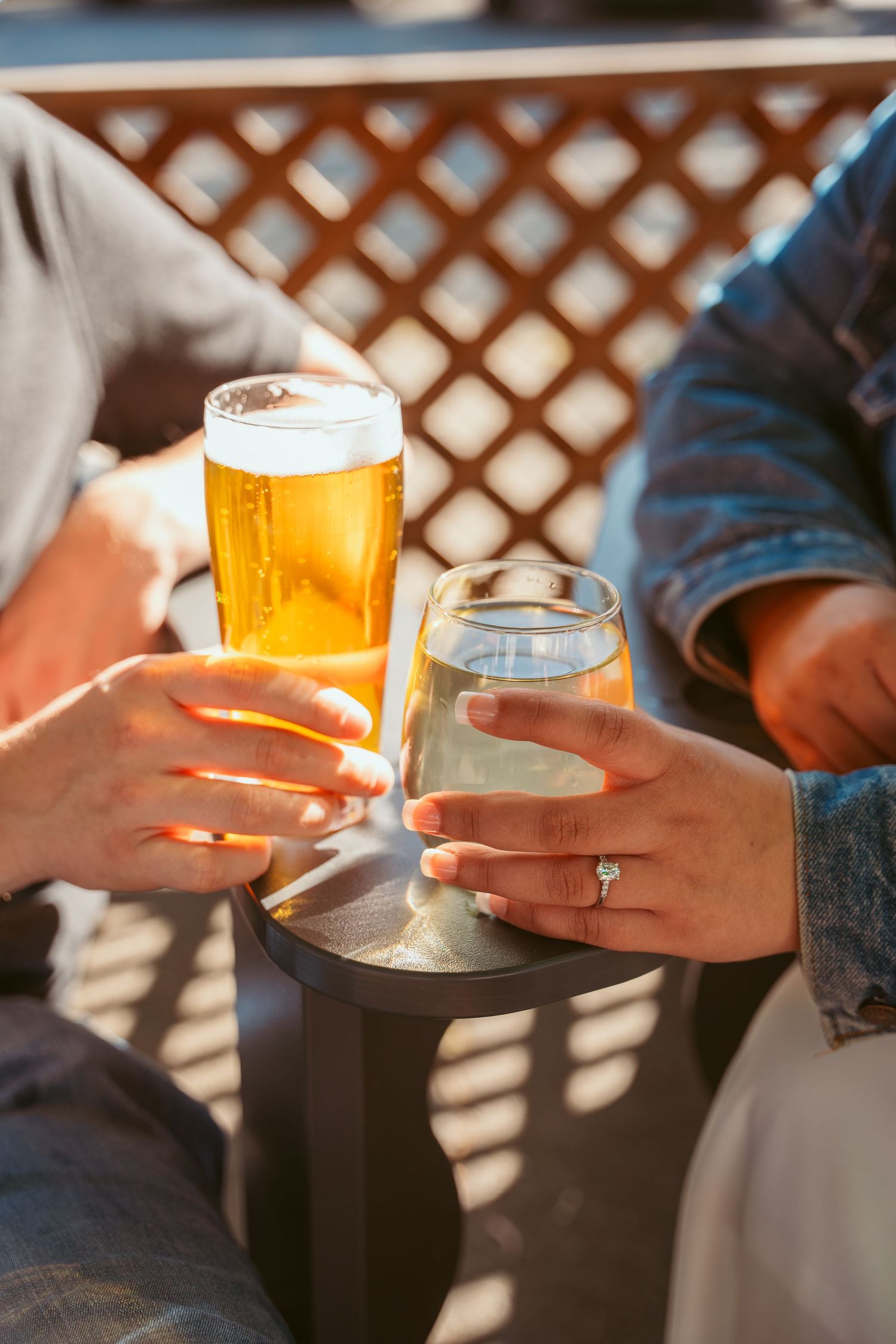 Hands hold drinks and glasses during a sunny outdoor gathering.