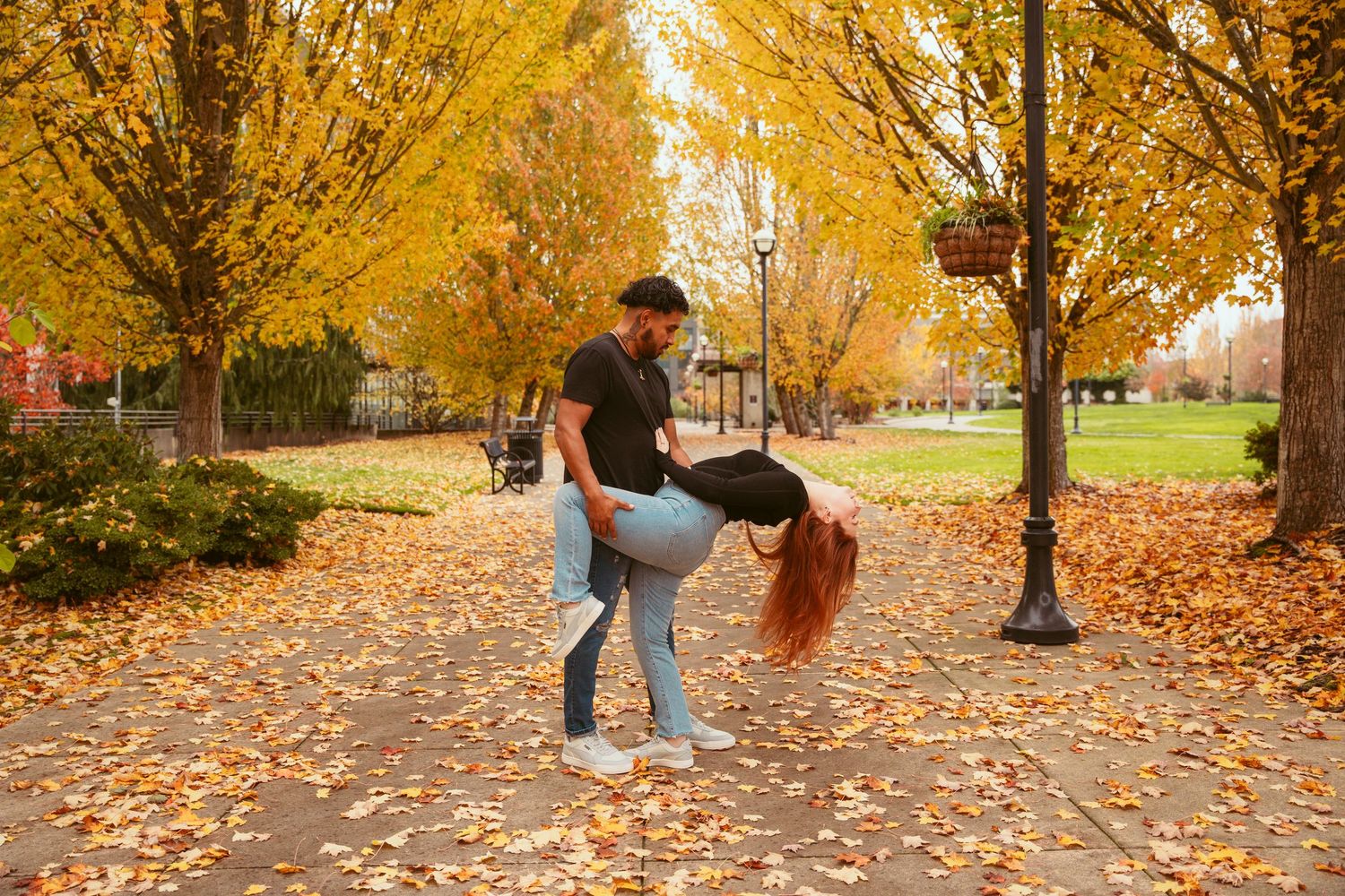 Couple enjoying a romantic autumn day under golden trees with fallen leaves scattered on the ground.