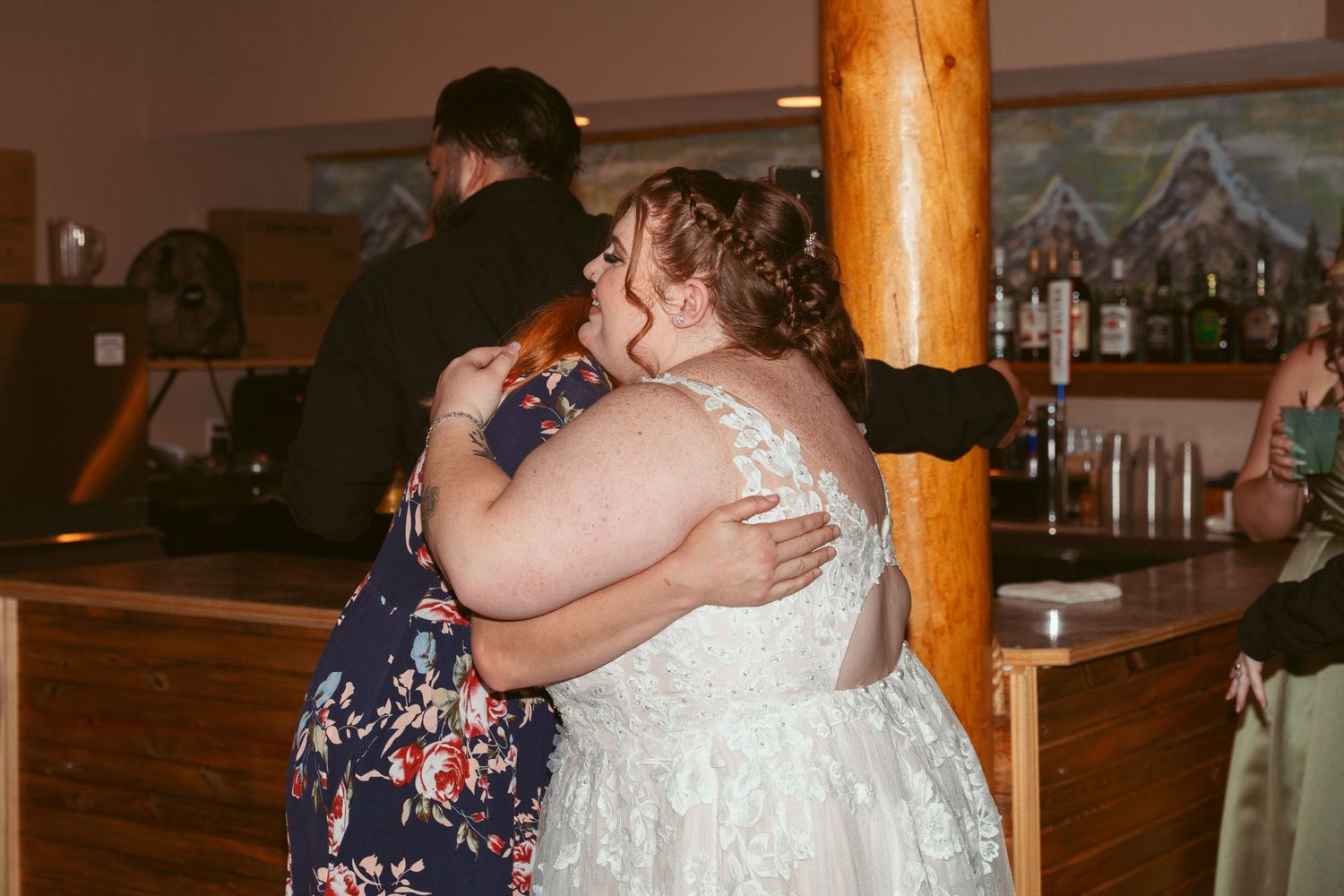 Two people embrace on the dance floor during a wedding reception in a rustic venue with wooden beams.