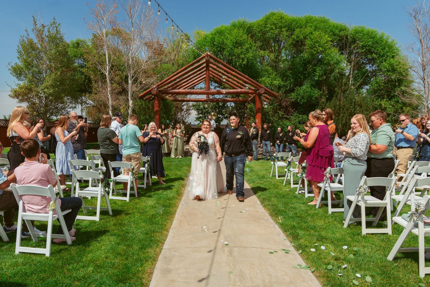 White chairs arranged outdoors on a green lawn for a garden wedding ceremony under blue skies.
