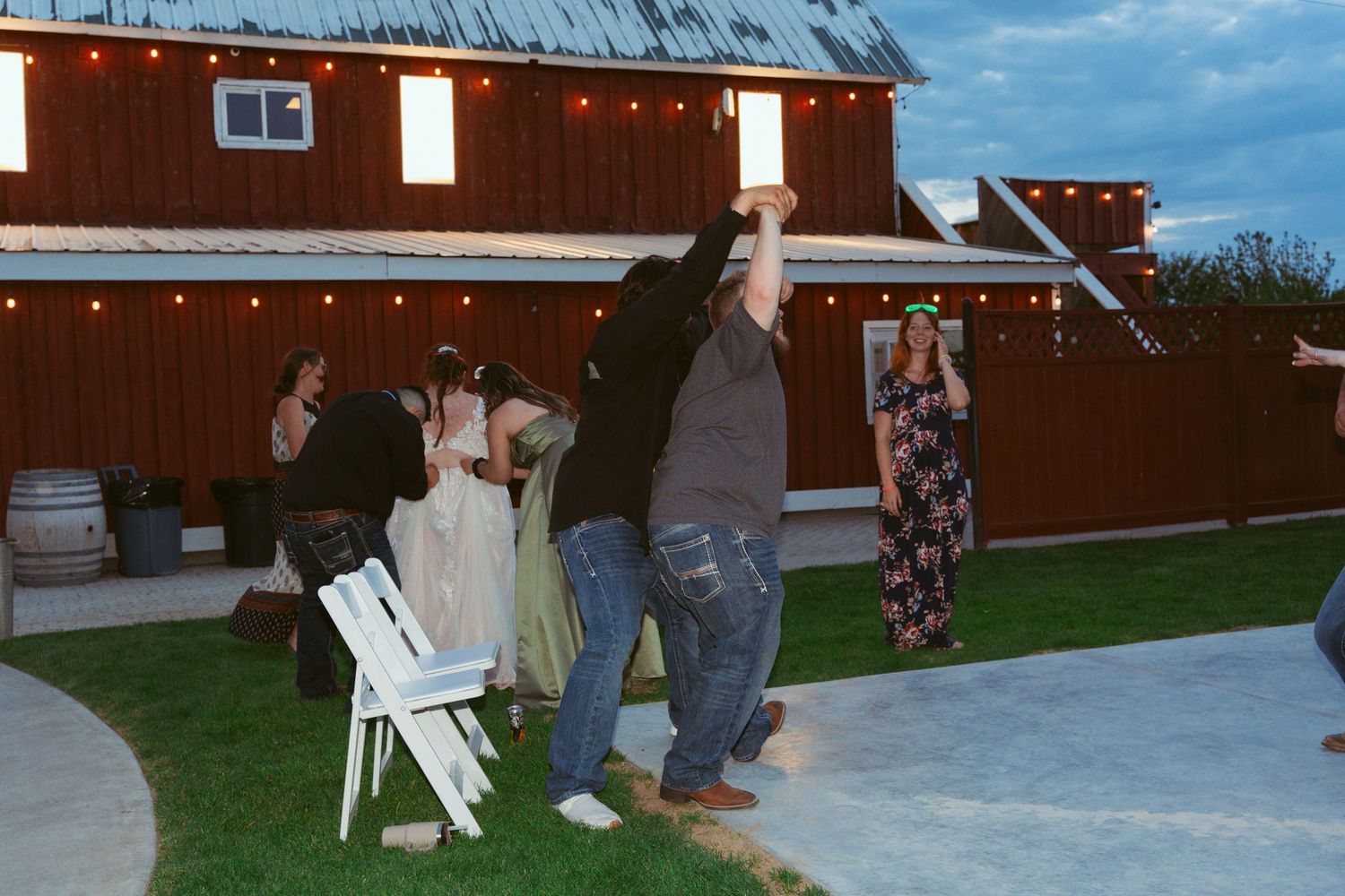 Outdoor wedding celebration with guests dancing on a patio near a rustic barn venue.