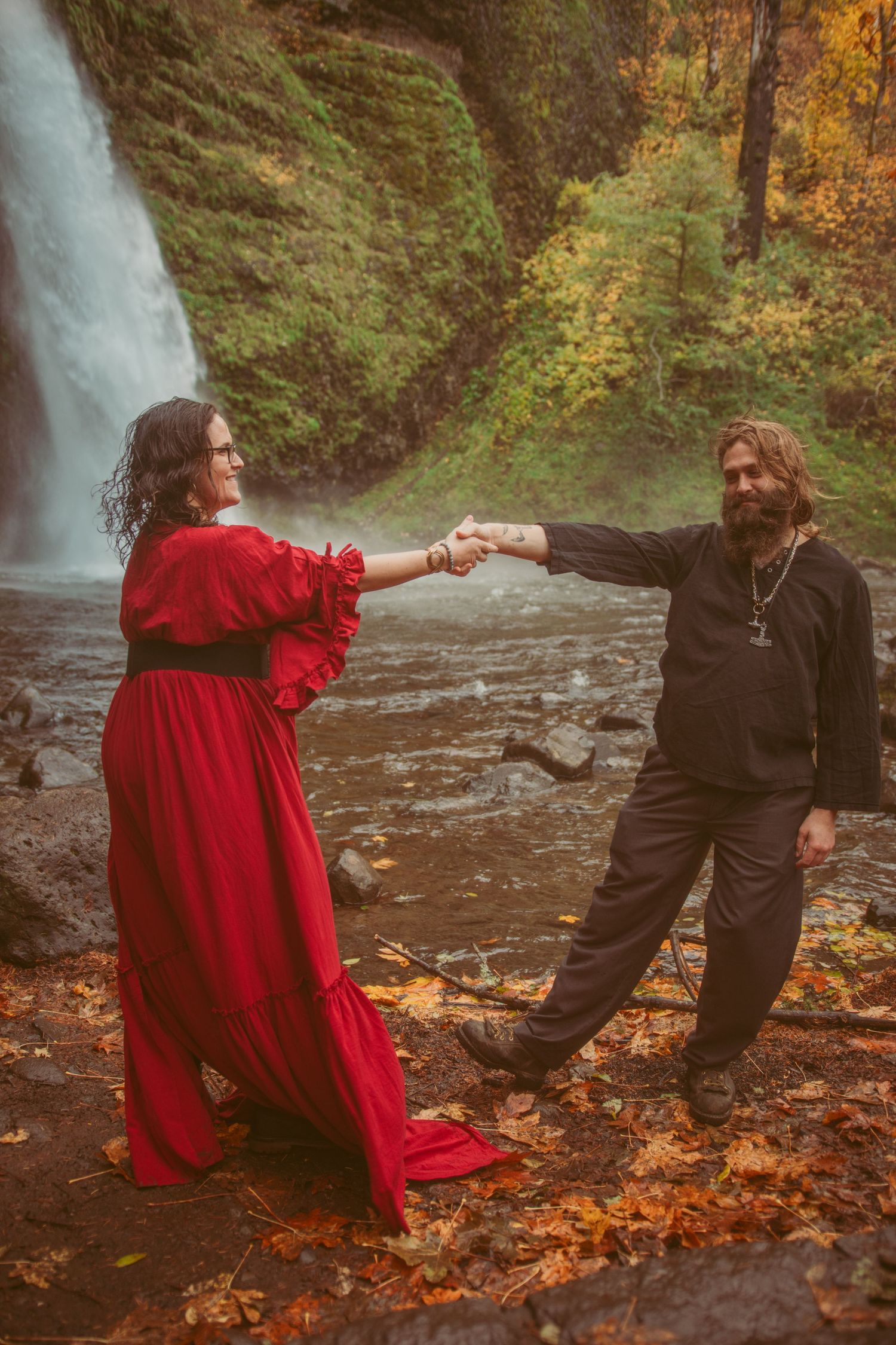 A couple performs a romantic dance sequence by a waterfall with autumn foliage on the ground.