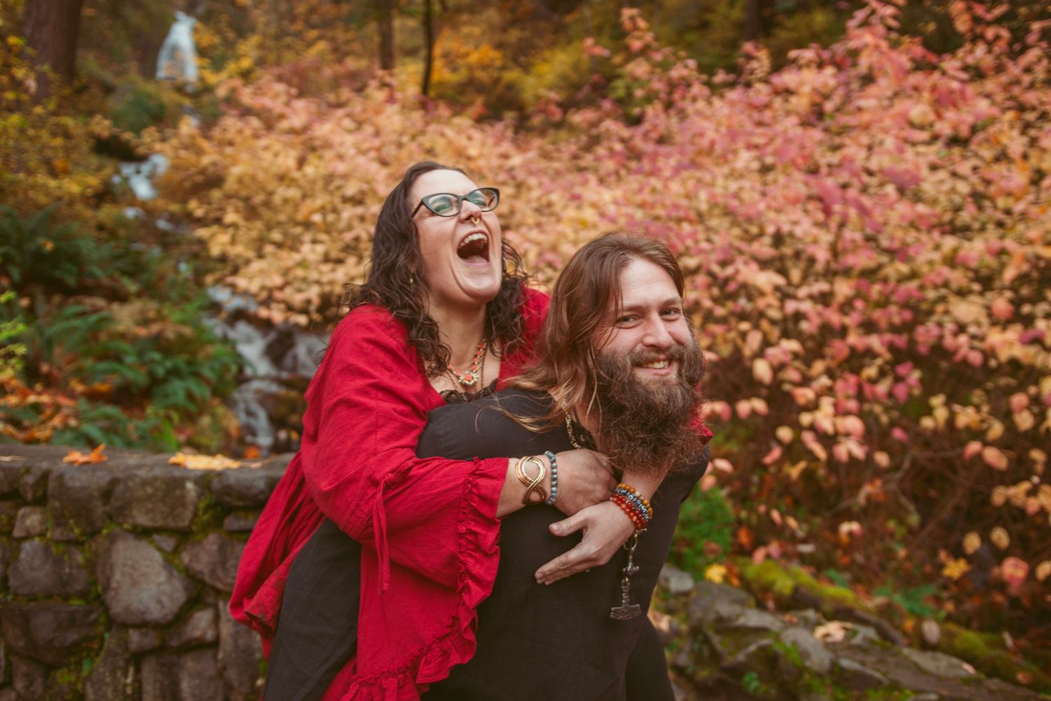 Joyful moment captured against vibrant autumn foliage and stone wall backdrop.