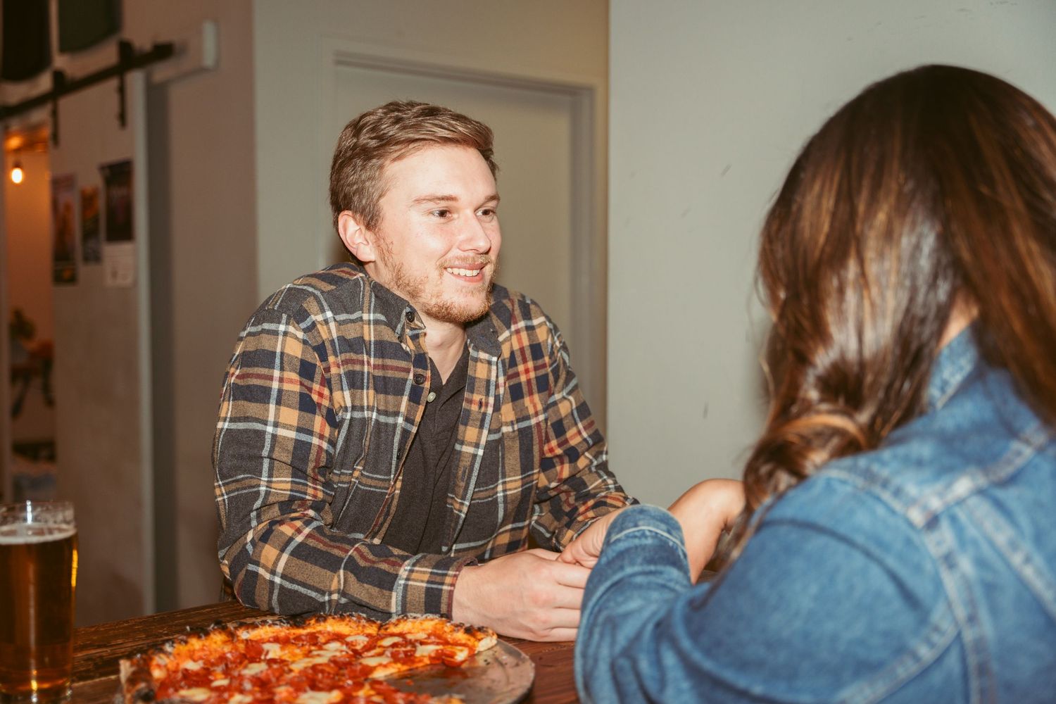 Casual dining scene with people enjoying pizza and drinks at a wooden table.