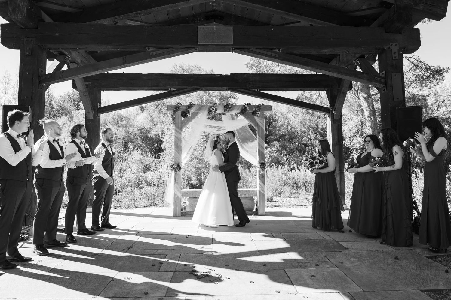 Wide angle view of a wedding ceremony under a covered outdoor pavilion with guests seated.