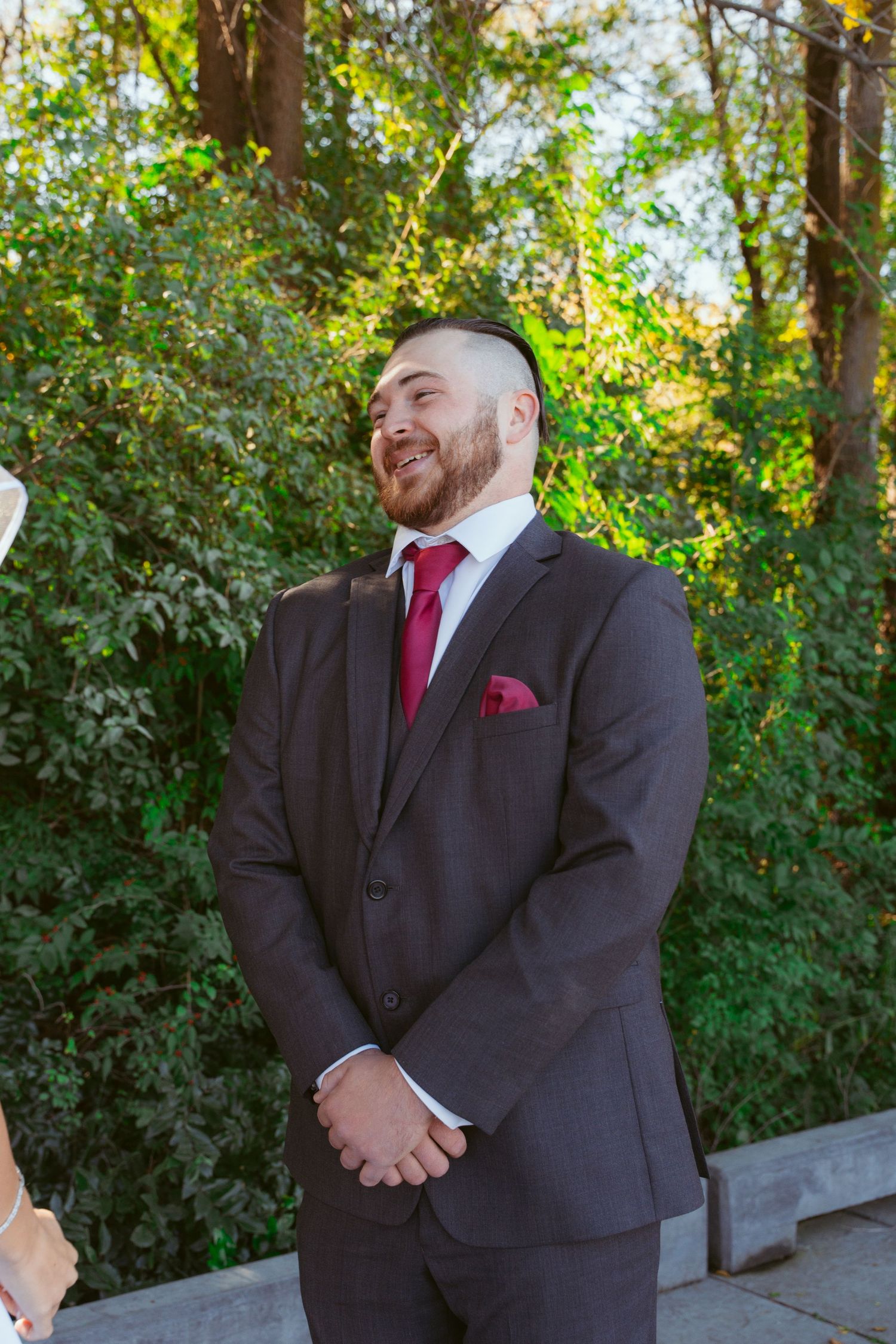 Groom in dark suit with burgundy tie smiling during first look moment.