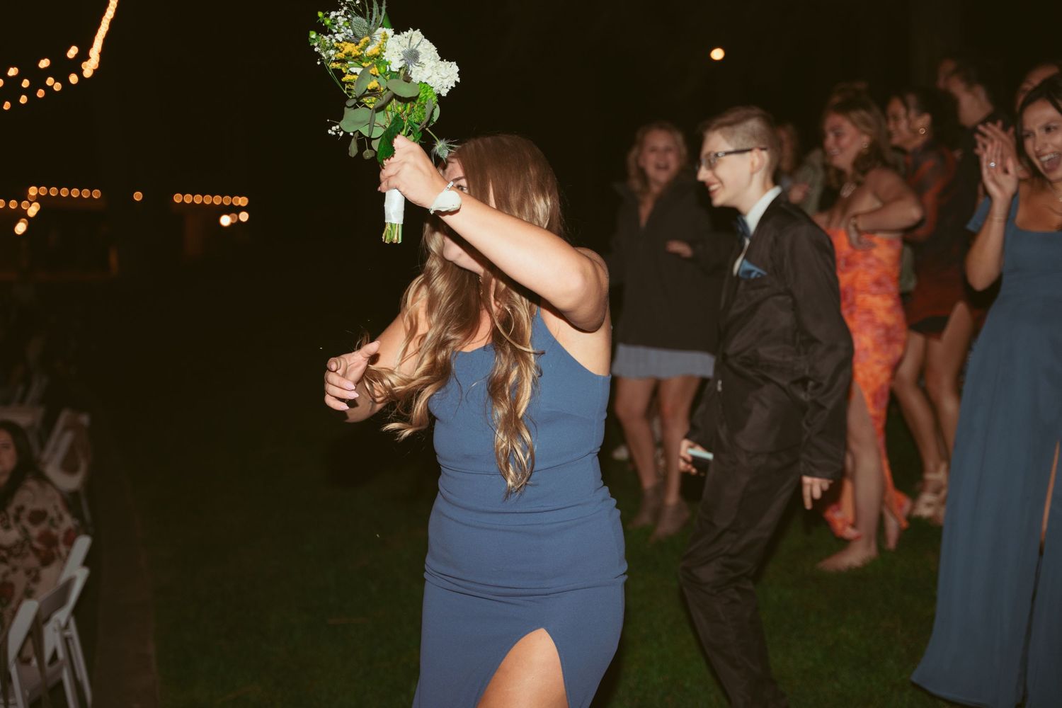 Wedding guests dancing at an outdoor reception under twinkling lights.