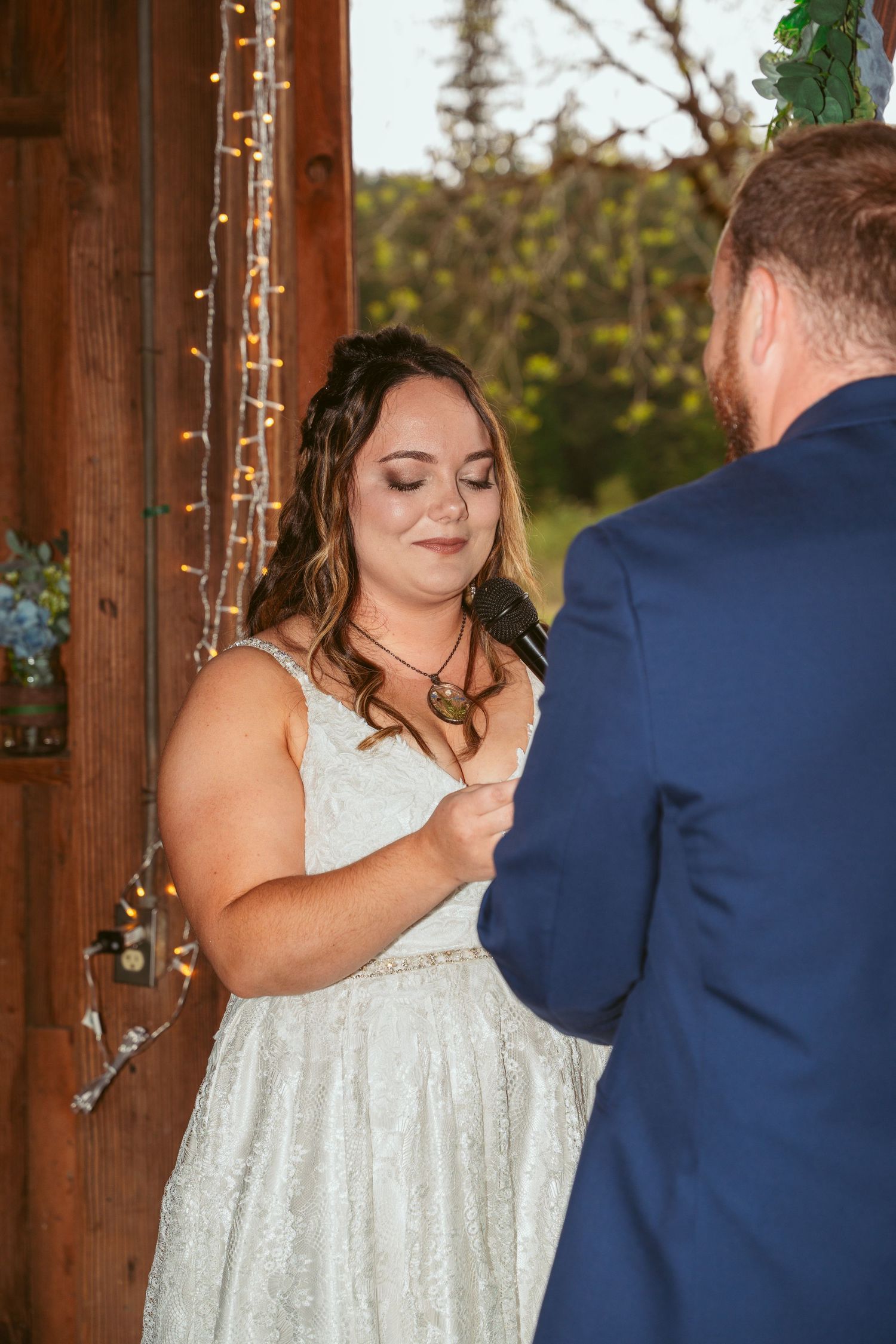 Emotional wedding ceremony moment in rustic barn with string lights and natural lighting.