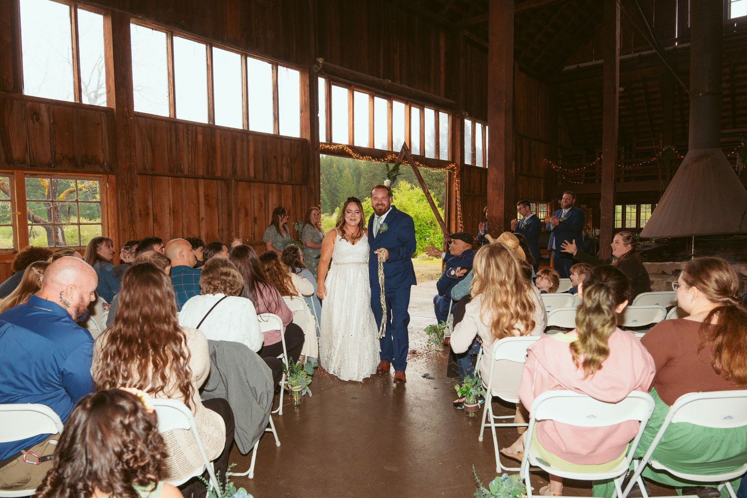 Guests attending a barn wedding ceremony with sunlight filtering through wooden slat walls.
