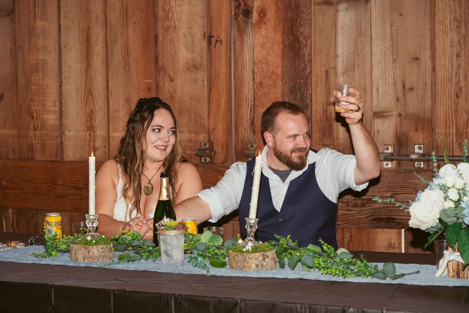 Wedding party members delivering speeches at reception in rustic barn venue.