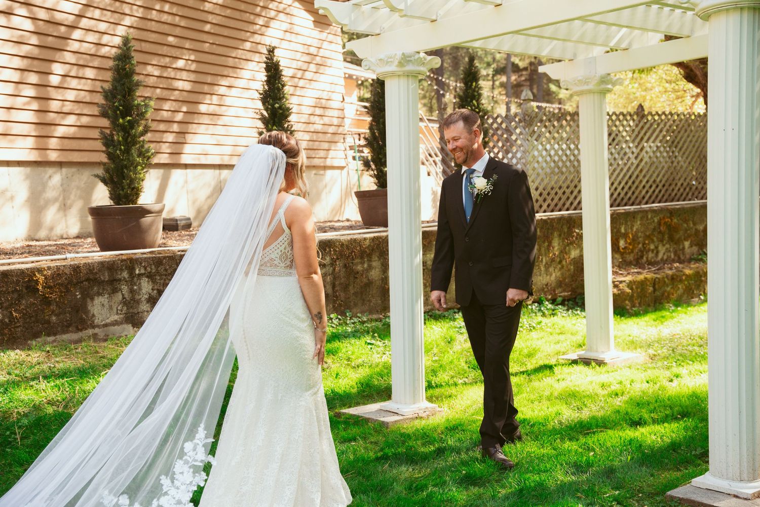 A romantic wedding couple poses in front of white gazebo columns on a sunny spring day.