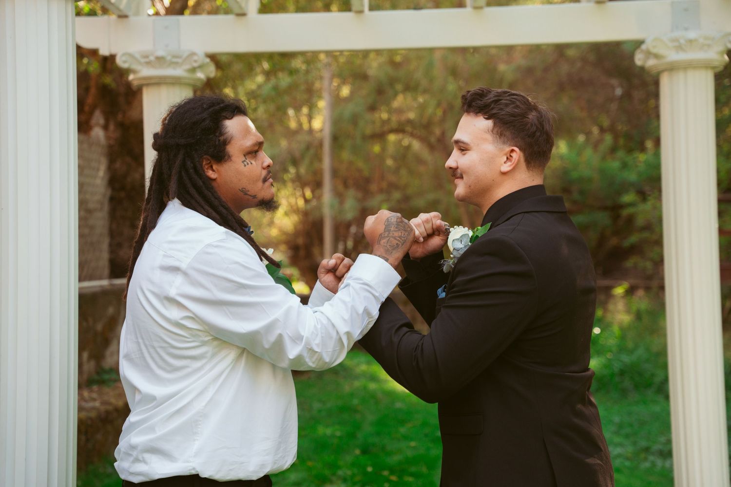 Playful interaction between two people in formal attire beneath a white pergola structure.