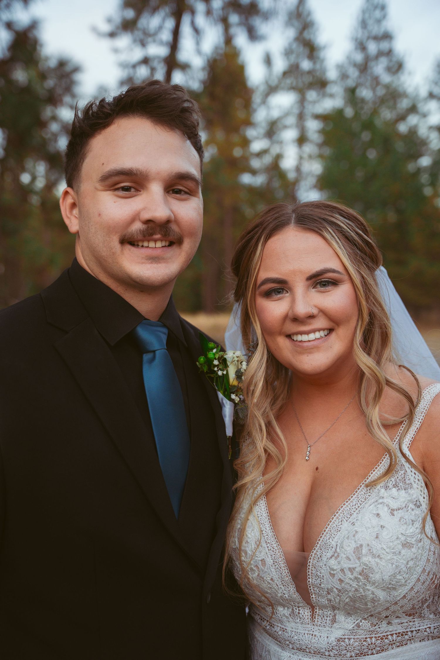 Wedding couple poses outdoors among pine trees during sunset photo session.