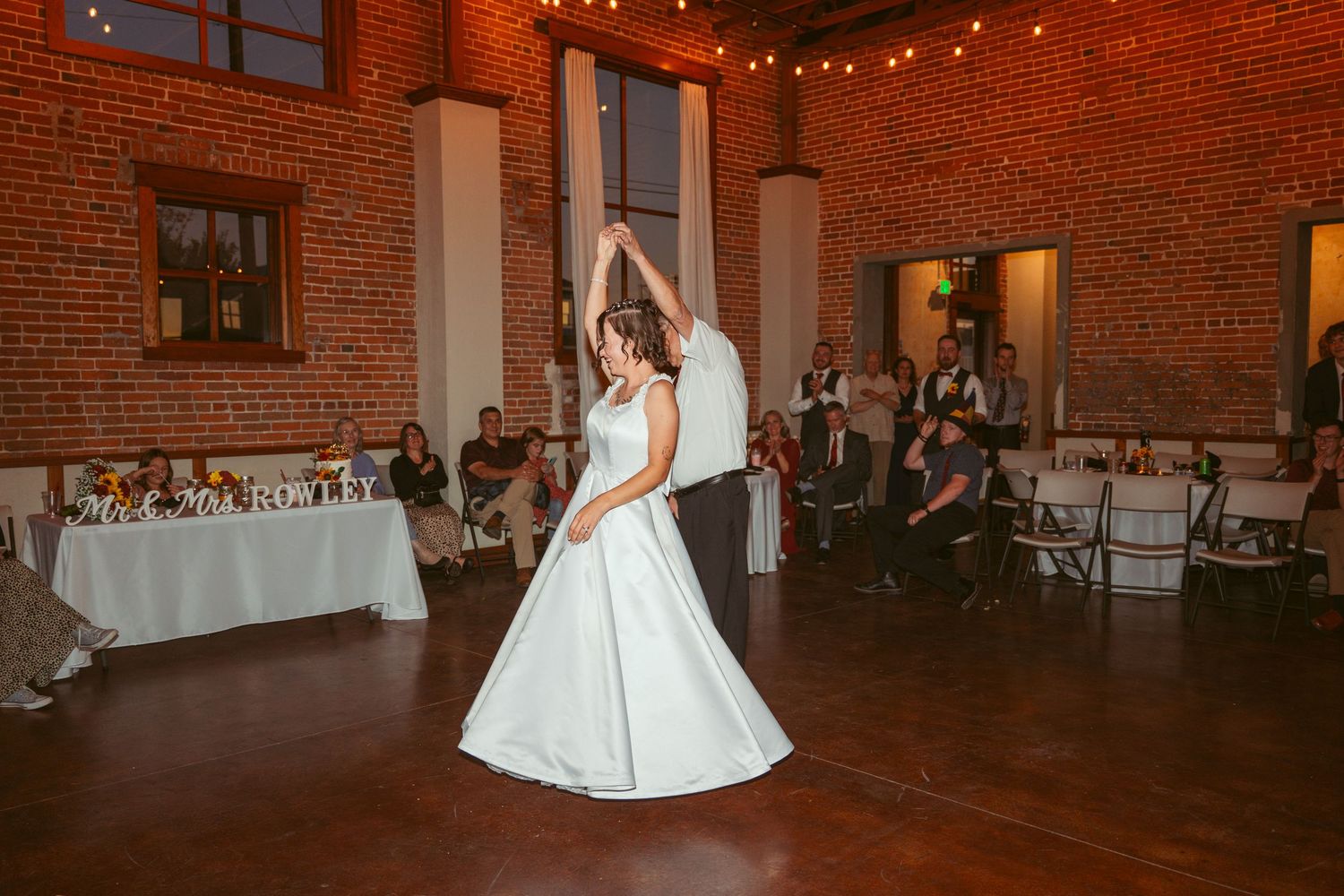 Couples dancing at an elegant wedding venue with exposed brick walls and ambient lighting.