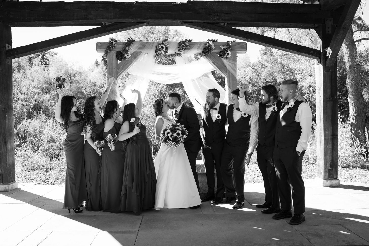 Black and white panoramic wedding party photo under covered outdoor venue.