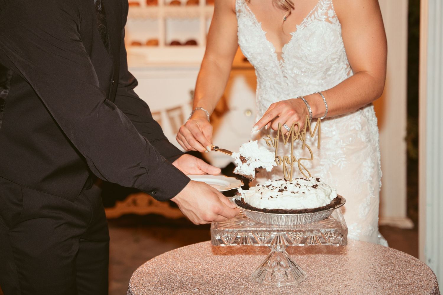 Close-up of hands cutting an elegant white wedding cake at a reception.