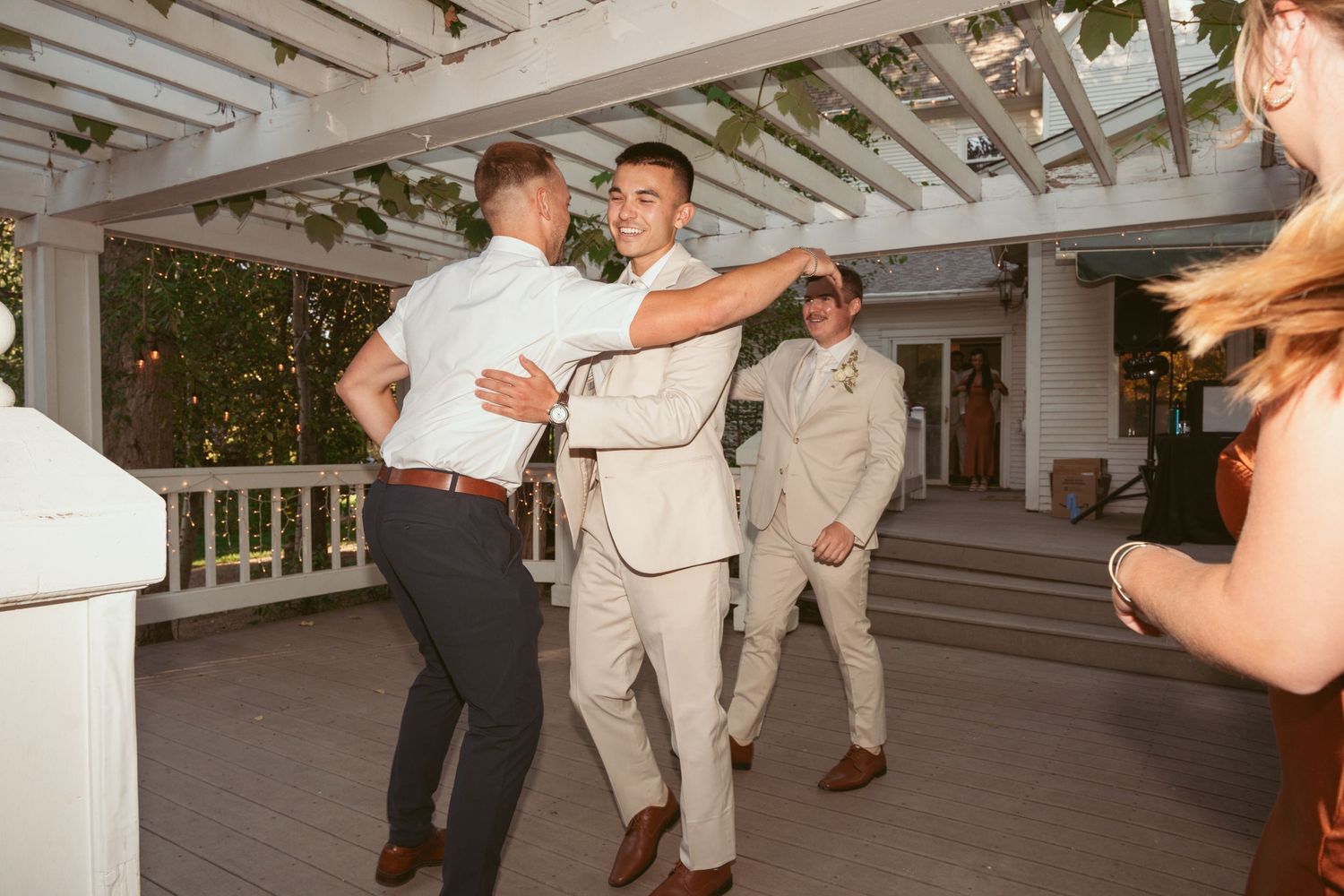 Guests dancing and celebrating on a white pergola-covered deck at an outdoor event.