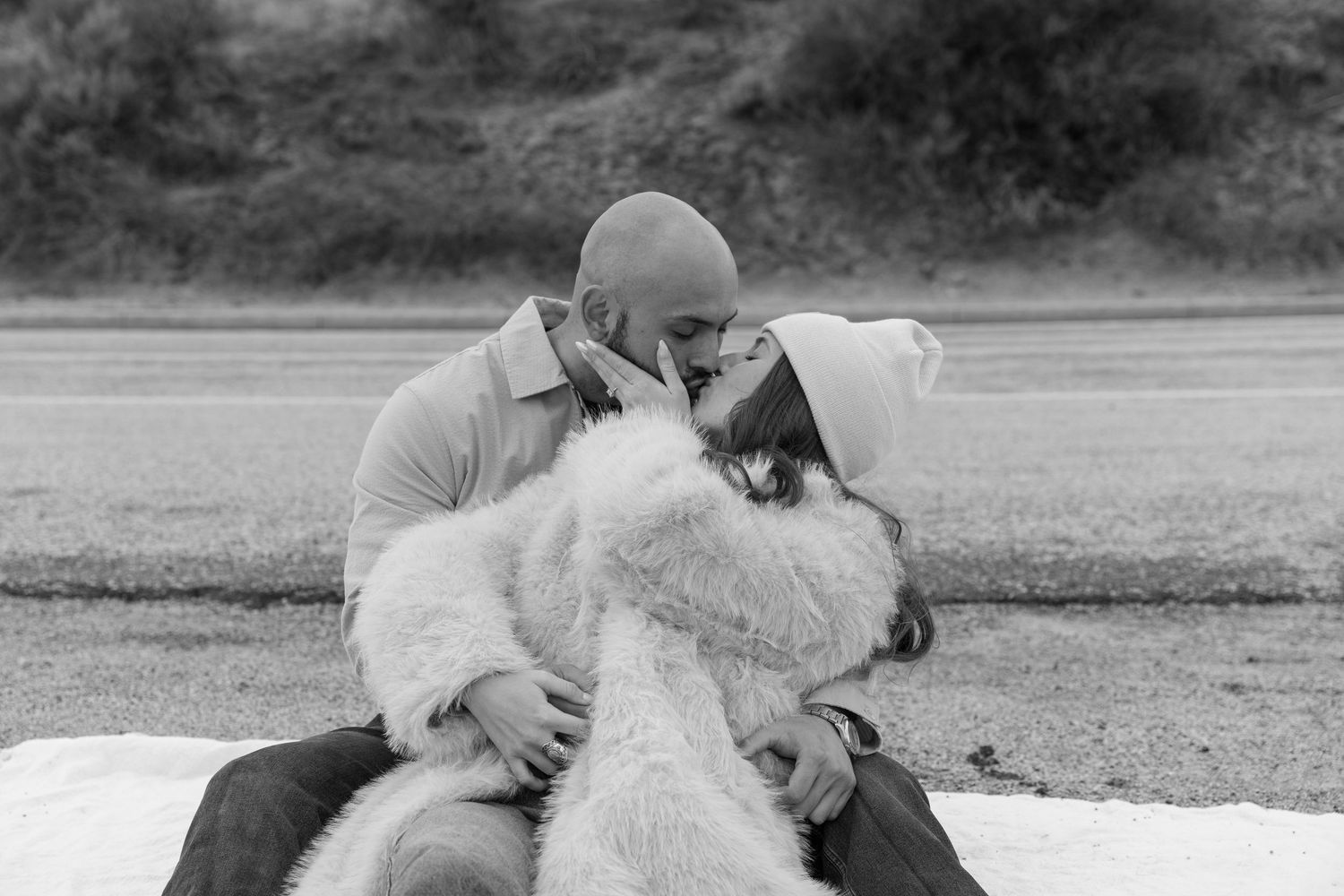 A black and white portrait of a couple sharing an intimate moment outdoors.