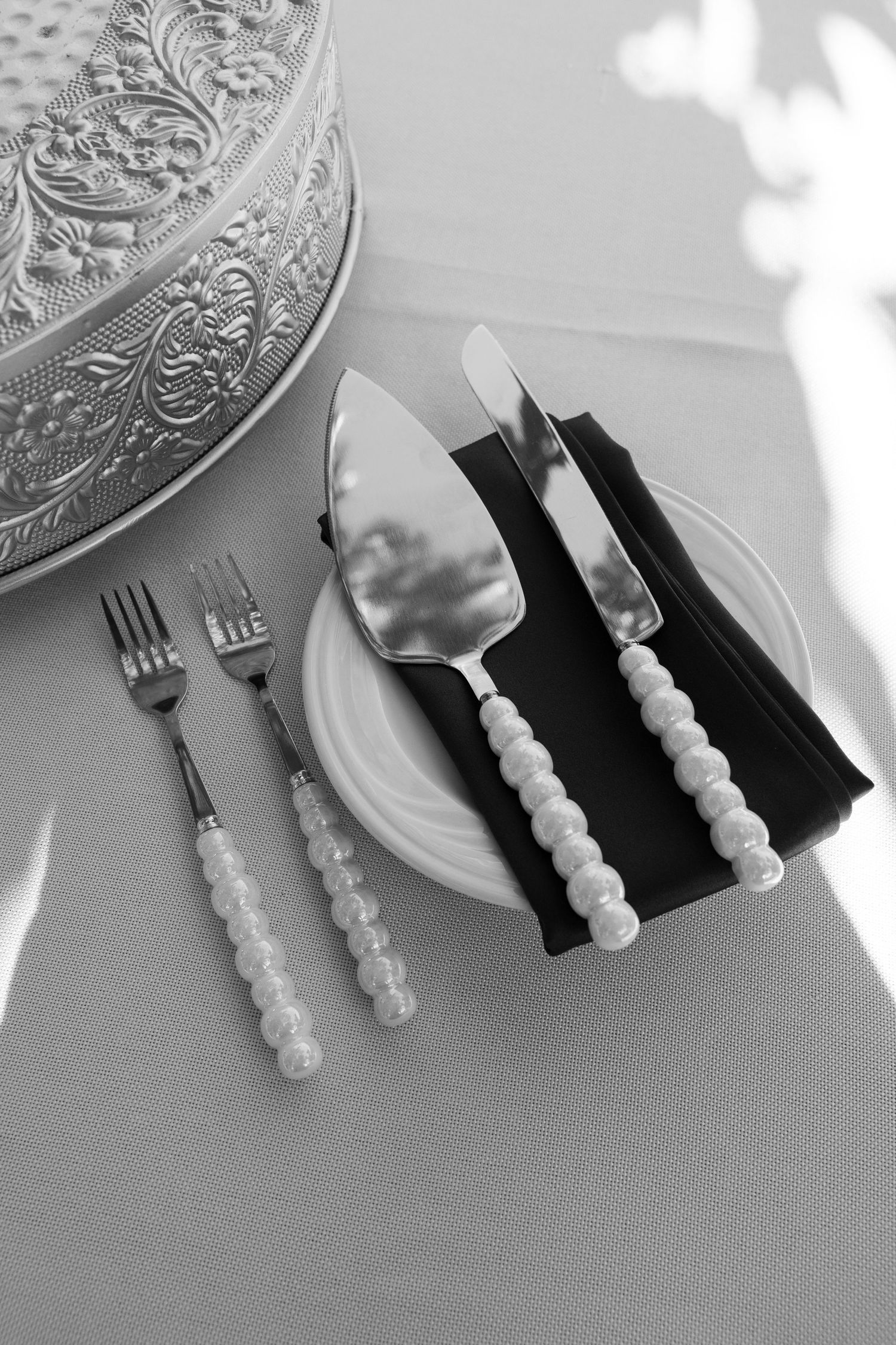 Black and white photo of elegant place settings with ornate silverware and napkins.