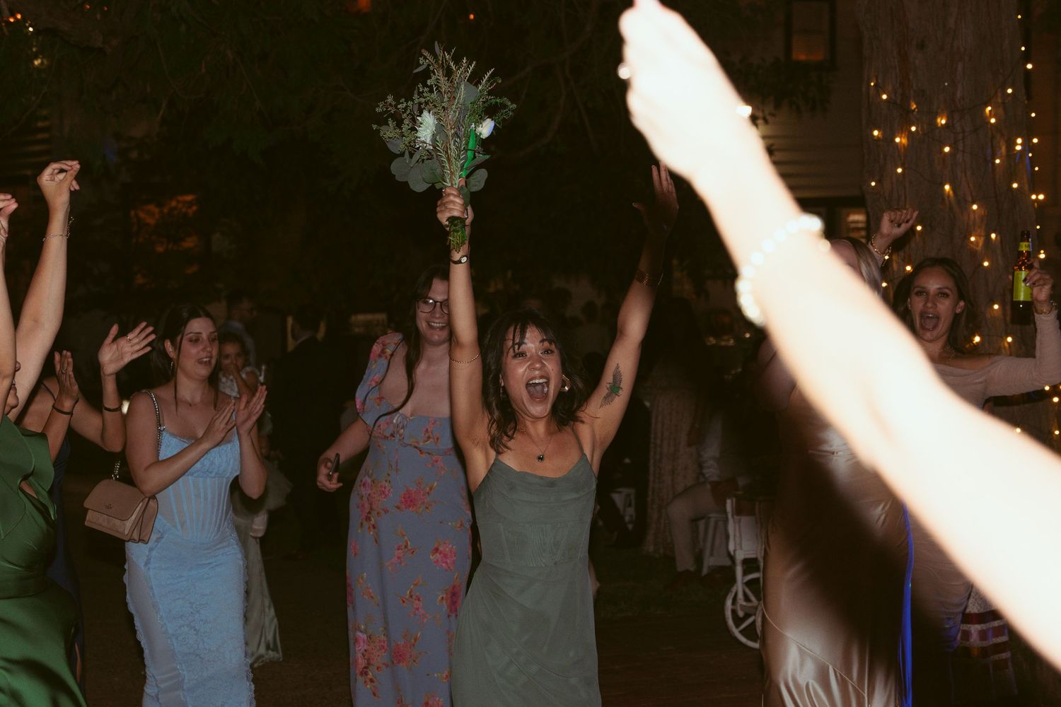 Guests celebrate on a dance floor beneath twinkling lights with arms raised in celebration.