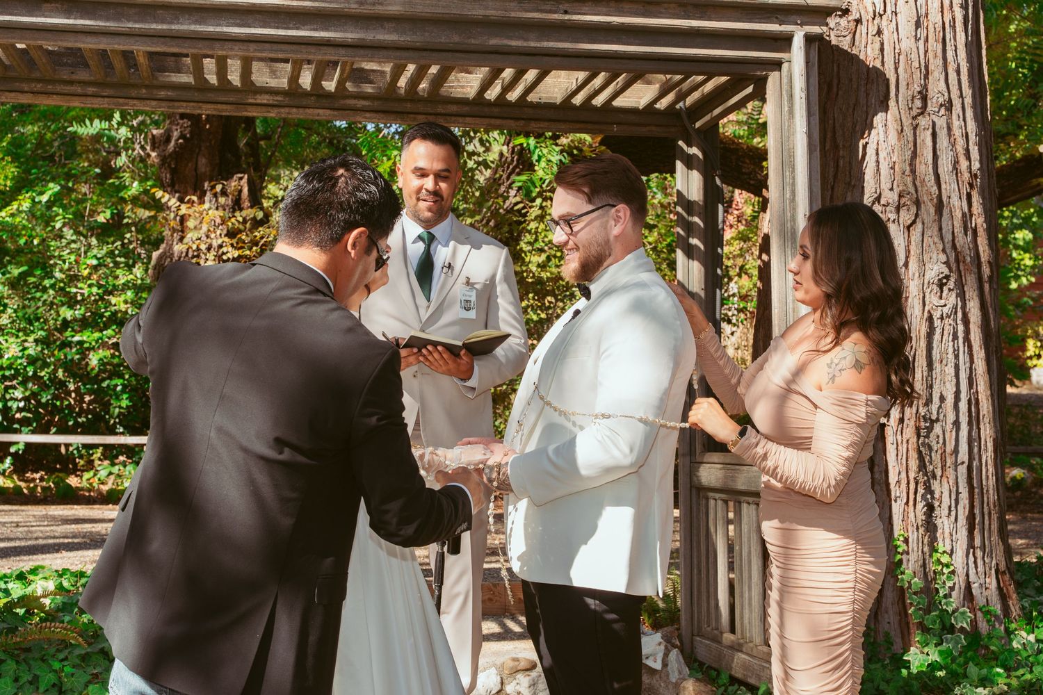 Couple shares a tender moment during their wedding ceremony in a rustic wooden gazebo surrounded by trees.