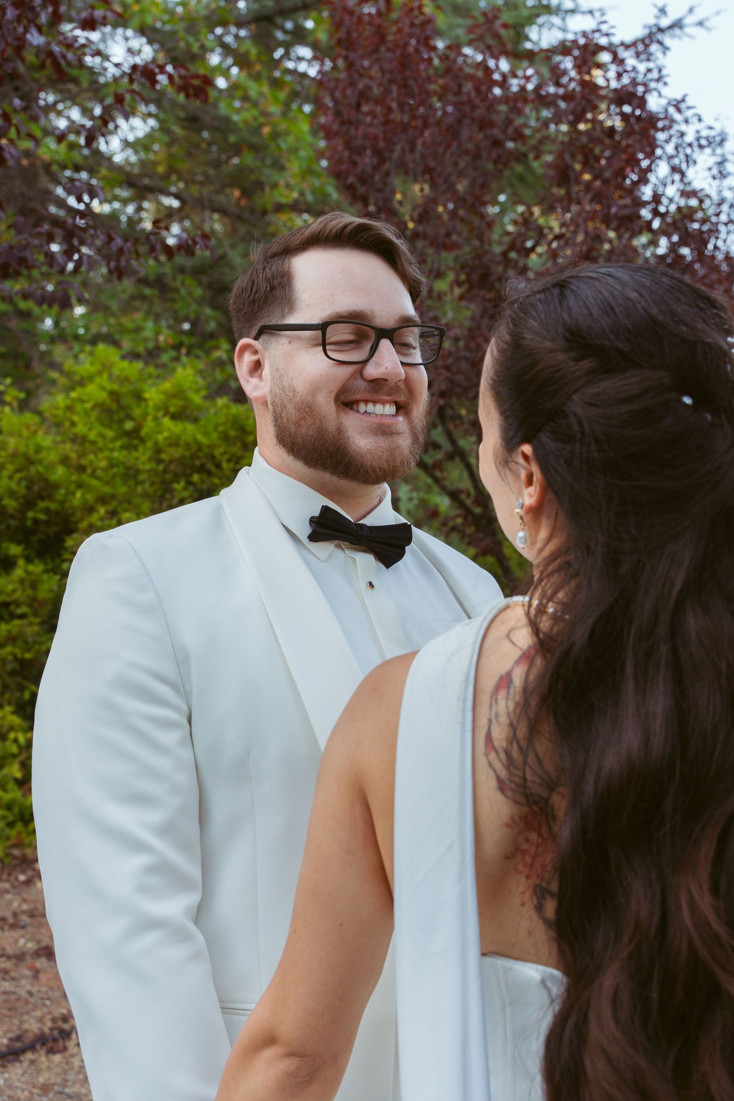 A couple shares an intimate moment in formal wedding attire against a natural outdoor backdrop.
