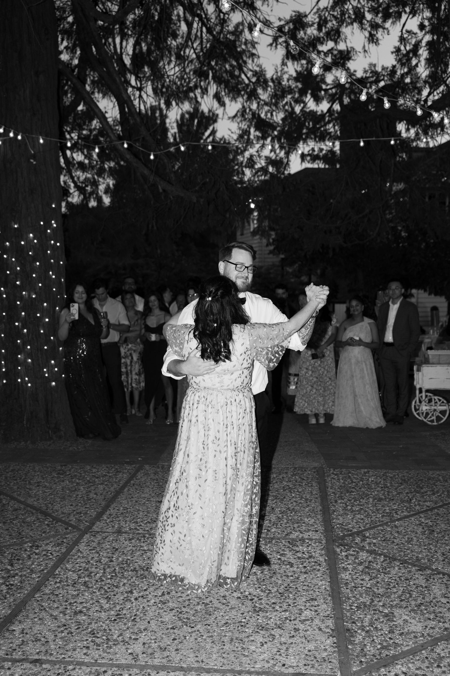 Couple shares a romantic dance under string lights at evening wedding reception.