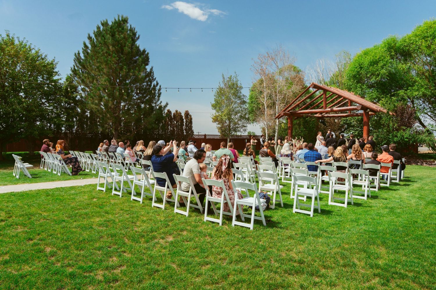 White chairs arranged on green lawn for outdoor wedding ceremony under blue sky.