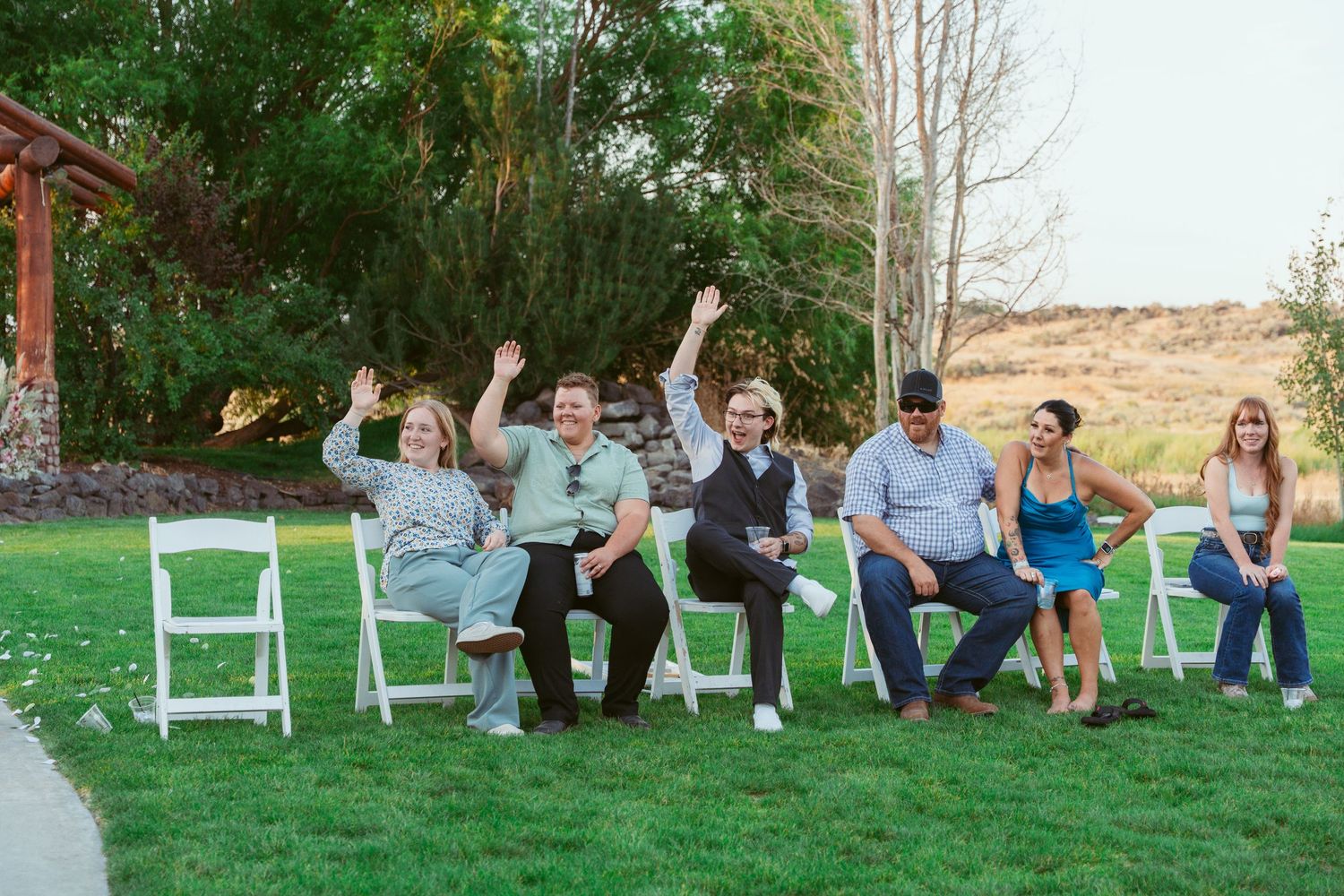 Wedding guests sit in white chairs on a lawn during an outdoor celebration.