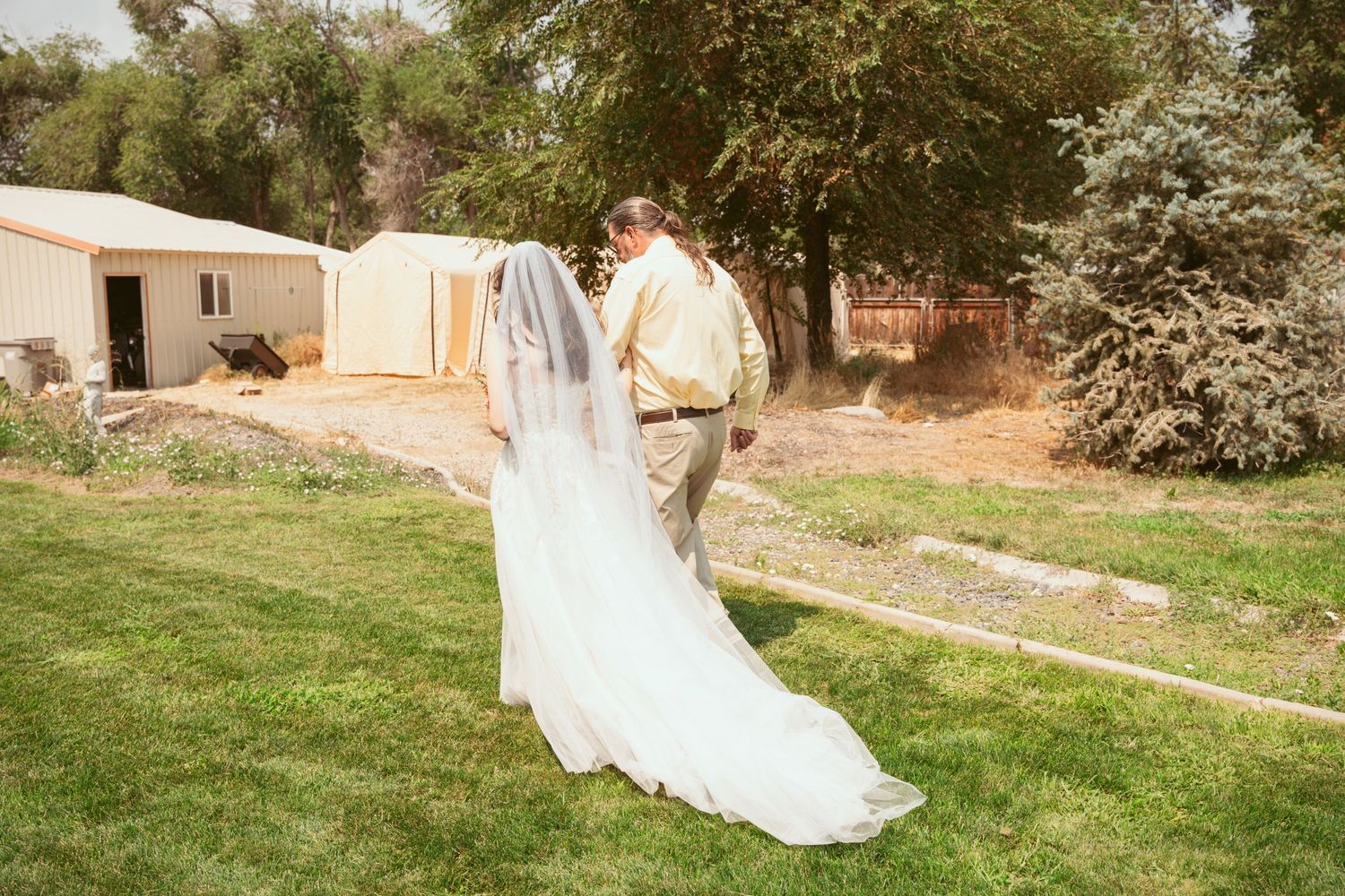 Panoramic view of newlyweds walking across a sunny lawn in wedding attire.