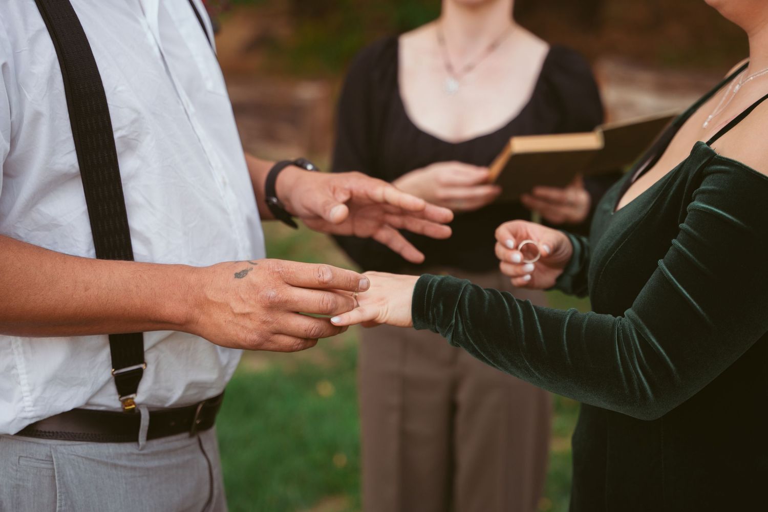 A couple exchanges rings during an outdoor wedding ceremony with an officiant present.